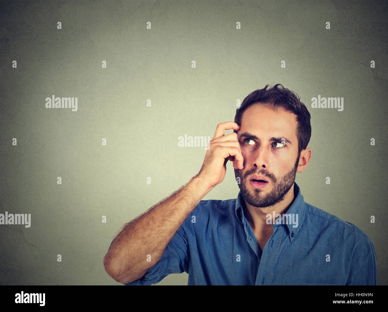 Closeup Portrait junger Mann kratzen Kopf tief etwa denken, etwas nachschlagen, auf graue Wand Hintergrund isoliert. Menschliche Mimik, em Stockfoto