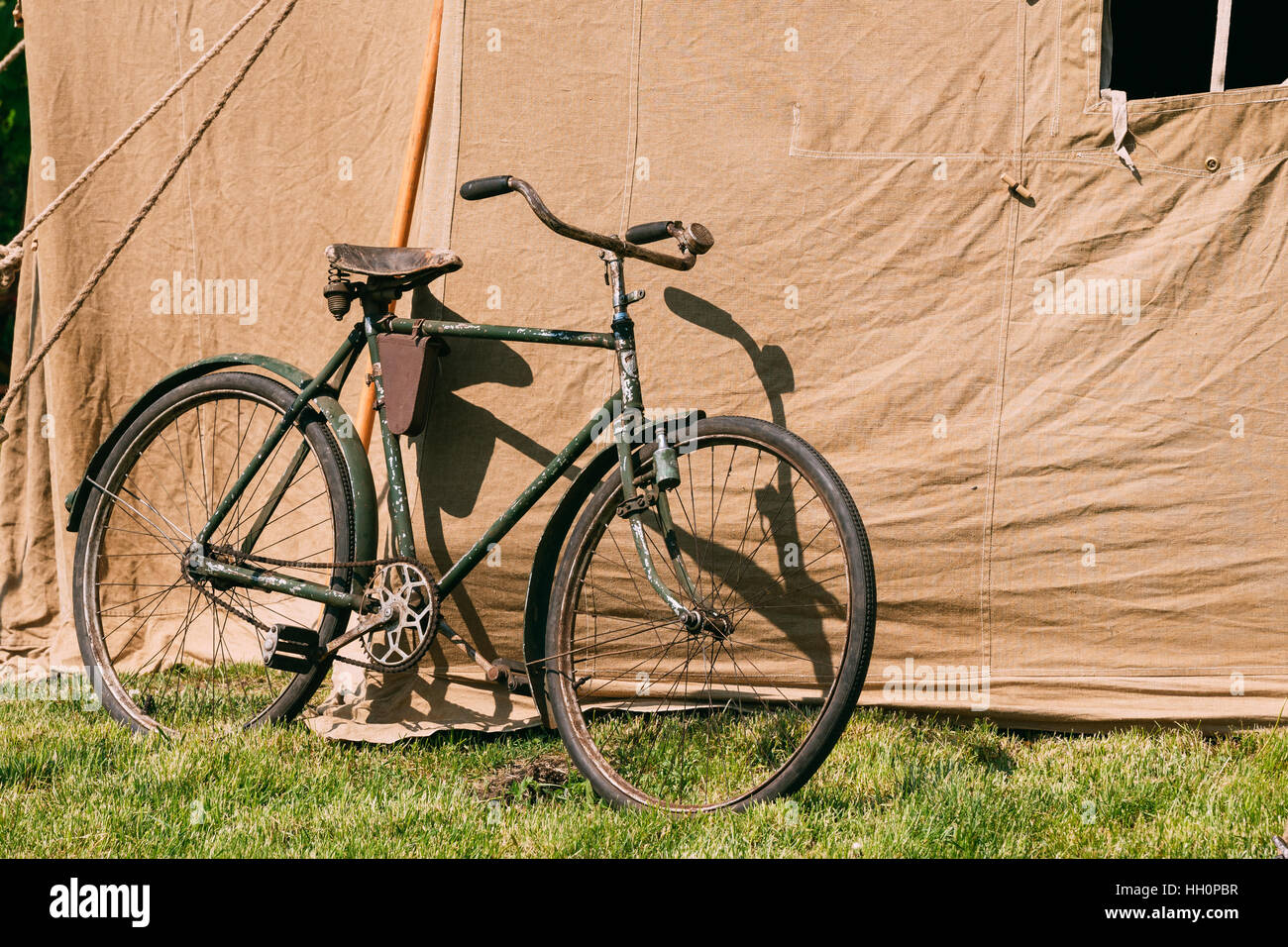 Das alte Rarität Fahrrad parkte neben der großen sowjetischen Militär Canvas Khaki Zelt auf dem grünen Rasen im sonnigen Sommer Wald. Stockfoto
