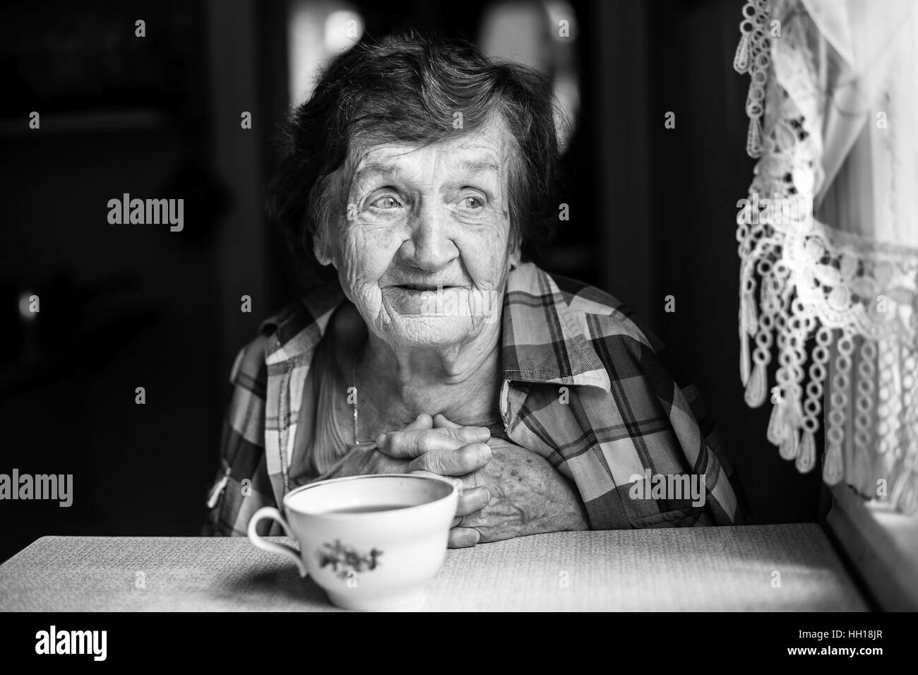 Ältere Frau, sitzt am Tisch im Haus Tee trinken. Schwarz-weiß-Porträt. Stockfoto