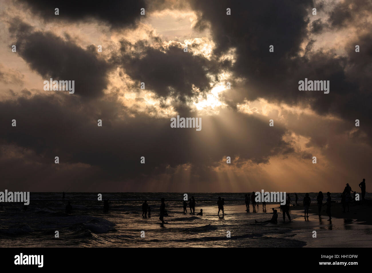 Menschen bei Gegenlicht auf Strand, Sonne, Strahlen von Licht, dunkle Wolken über Meer, Beruwela, Western Province, Sri Lanka Stockfoto