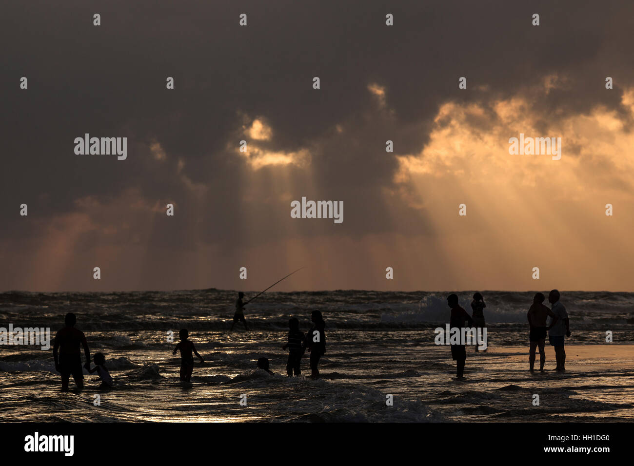 Menschen bei Gegenlicht am Strand, Sonnenstrahlen, dunkle Wolken über Meer, Beruwela, Western Province, Sri Lanka Stockfoto