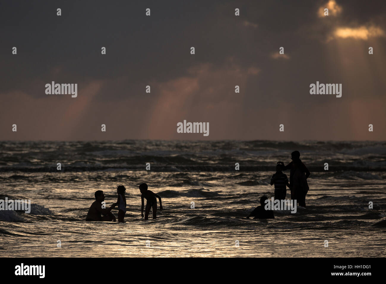 Menschen bei Gegenlicht im Wasser, Sonnenstrahlen, dunkle Wolken über Meer, Beruwela, Western Province, Sri Lanka Stockfoto