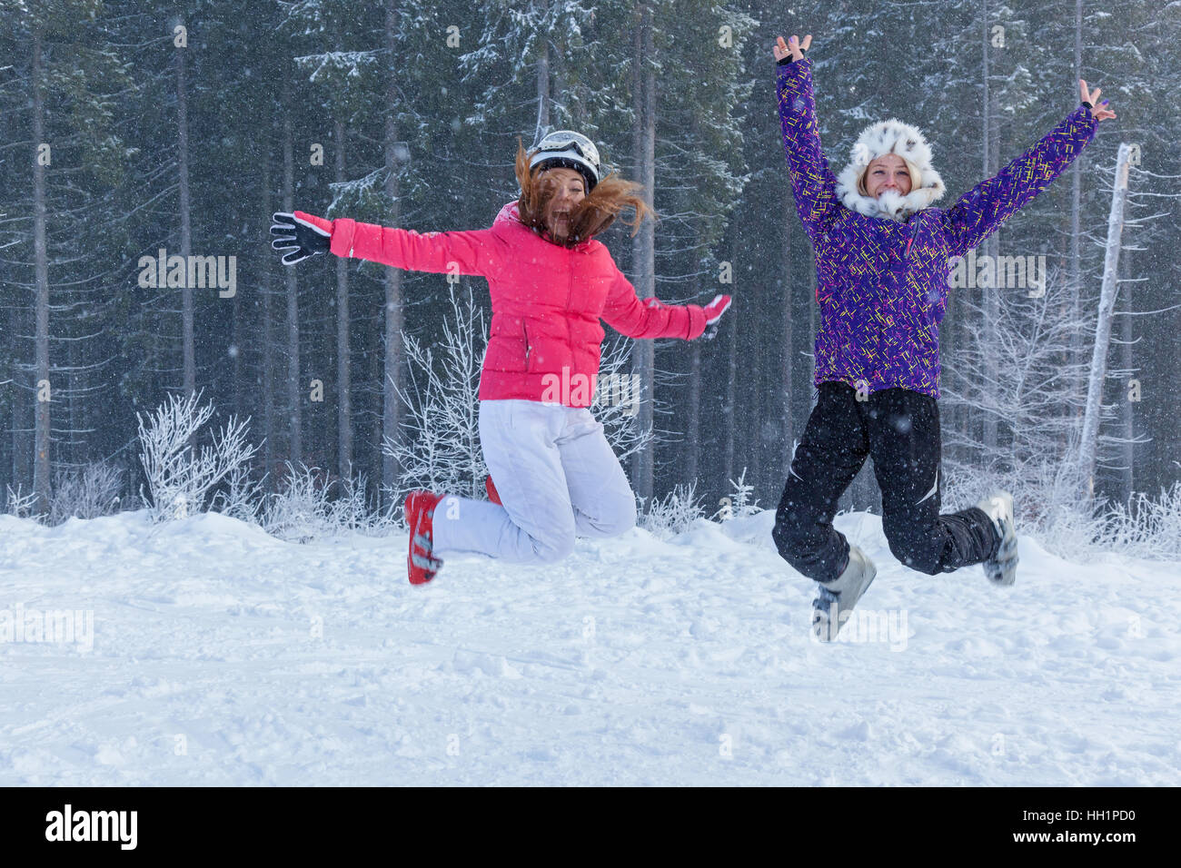 Ukraine Bukovel 17. Dezember 2015 Mädchen springen. Zwei lustige Mädchen springen im Schnee gegen schönen Wald in Bukovel, Ukraine. Stockfoto