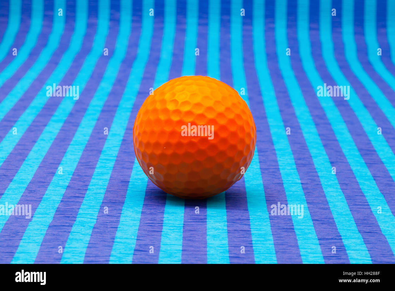 Orange Golfball auf blau gestreifte Tischdecke. Stockfoto