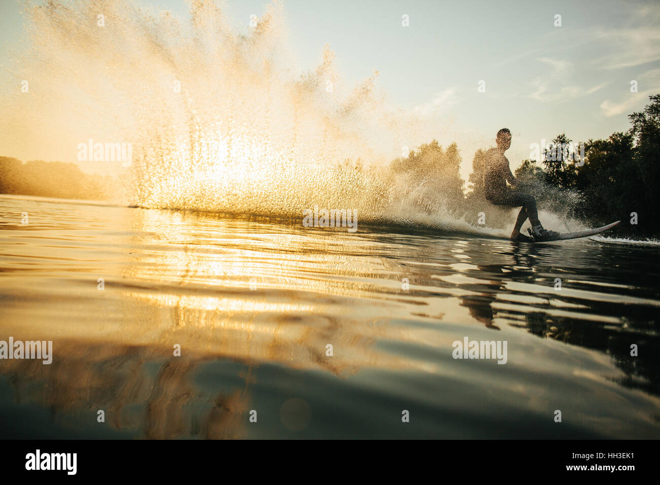 Niedrigen Winkel Schuss des Mannes Wakeboarding an einem See. Man Wasserski bei Sonnenuntergang. Stockfoto