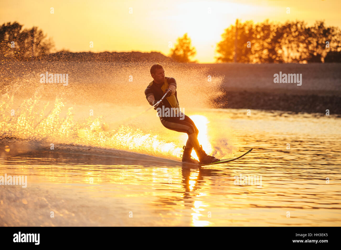 Im Freien Schuss des Mannes Wasserski bei Sonnenuntergang. Mann Wakeboarden an einem See. Stockfoto
