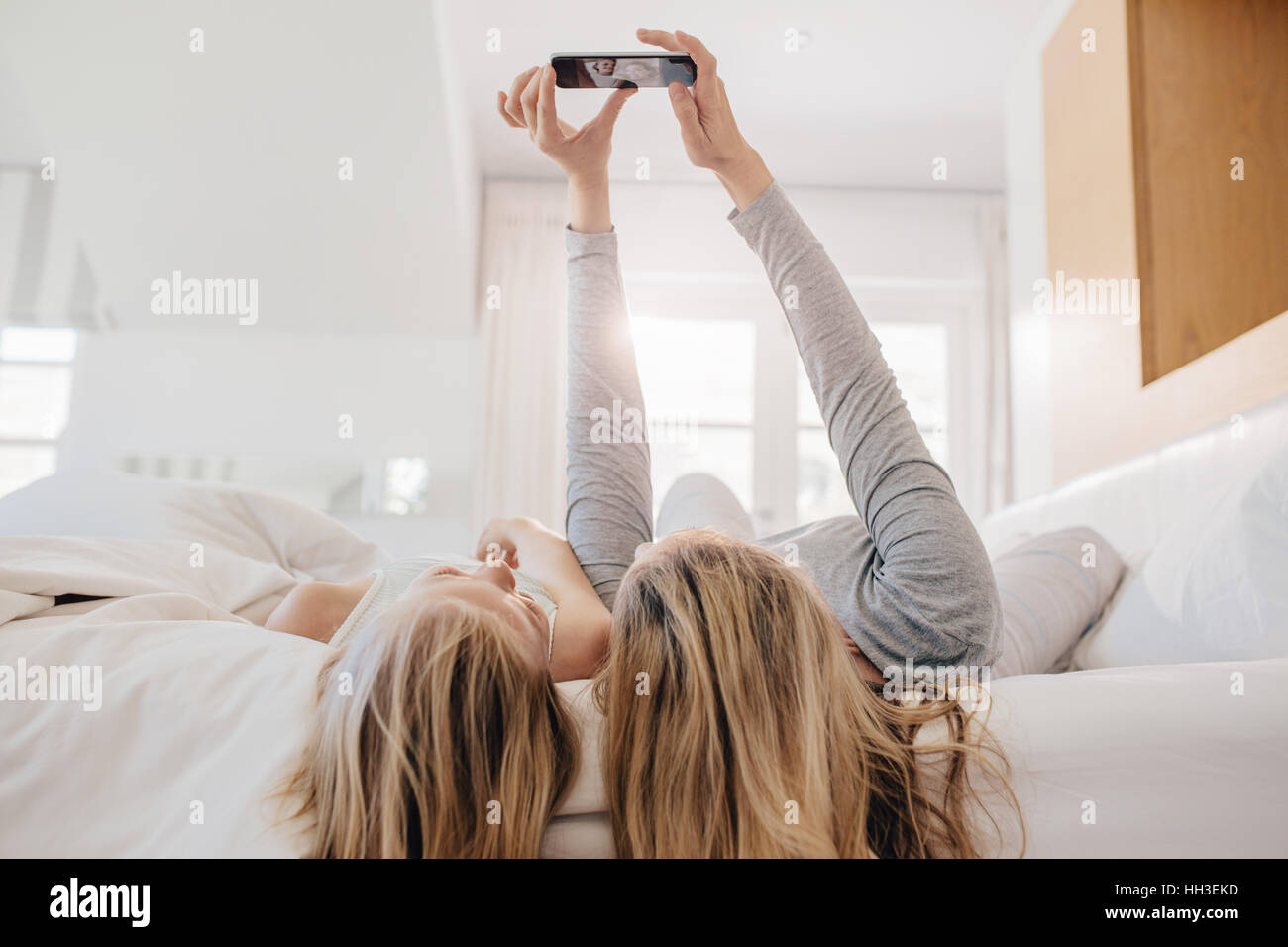 Mutter und Tochter am Bett liegen und unter Selbstbildnis mit Smartphone. Frau unter Selfie mit einem kleinen Mädchen im Schlafzimmer. Stockfoto