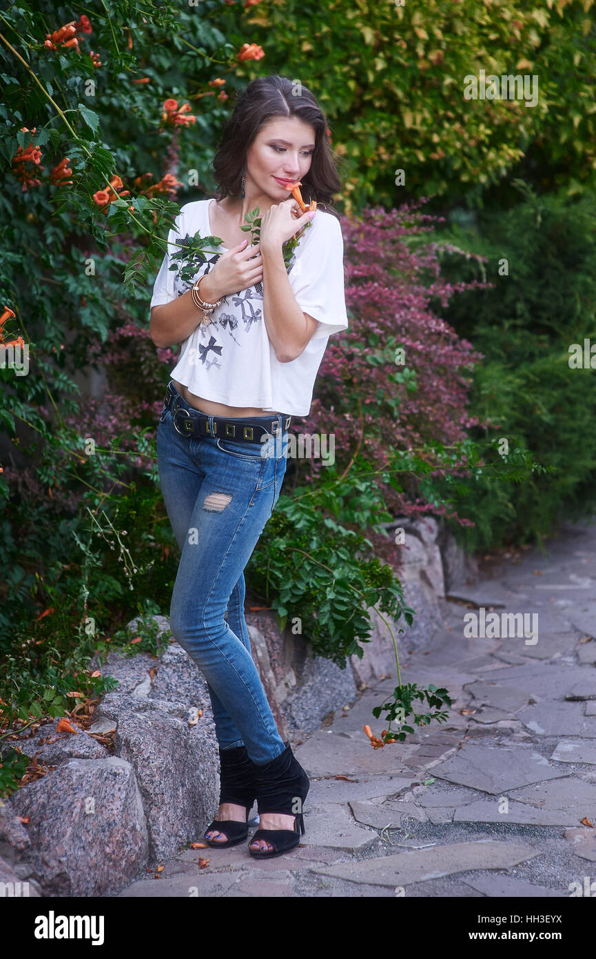 glückliche junge Frau posiert in einem Park in der Nähe von Blumen Stockfoto