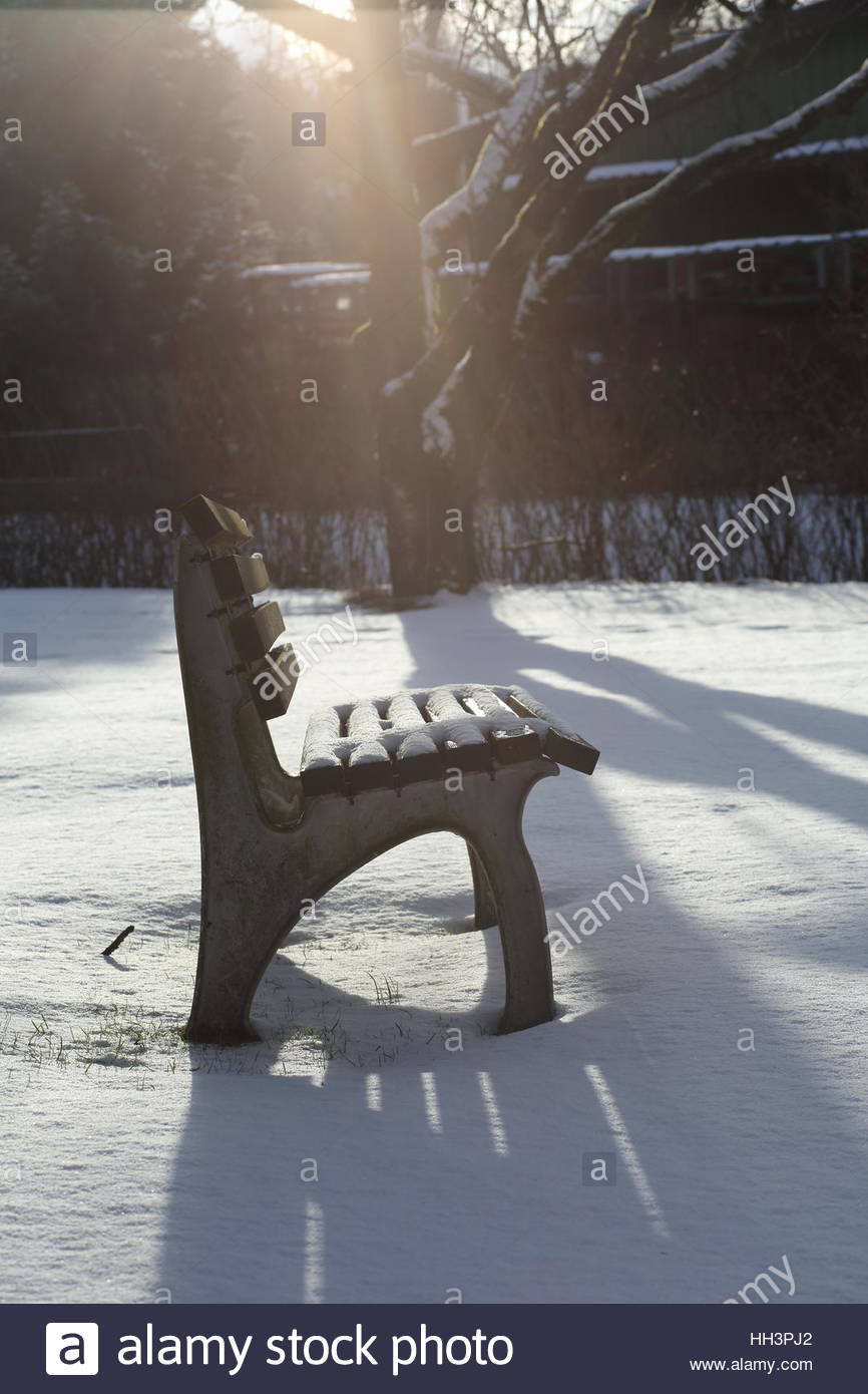 Eine Bank im Winterschnee in einem Garten in Bayern, während die Sonne scheint. Stockfoto