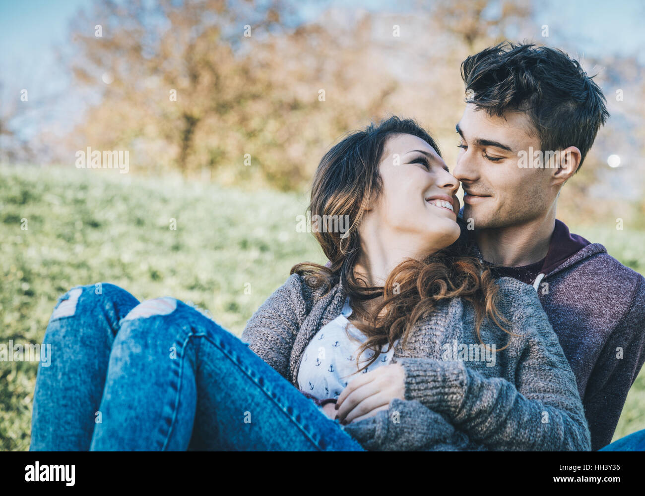 Glückliches junges Paar sitzen auf dem Rasen, umarmen und küssen im Freien, Liebe und Romantik Konzept Stockfoto