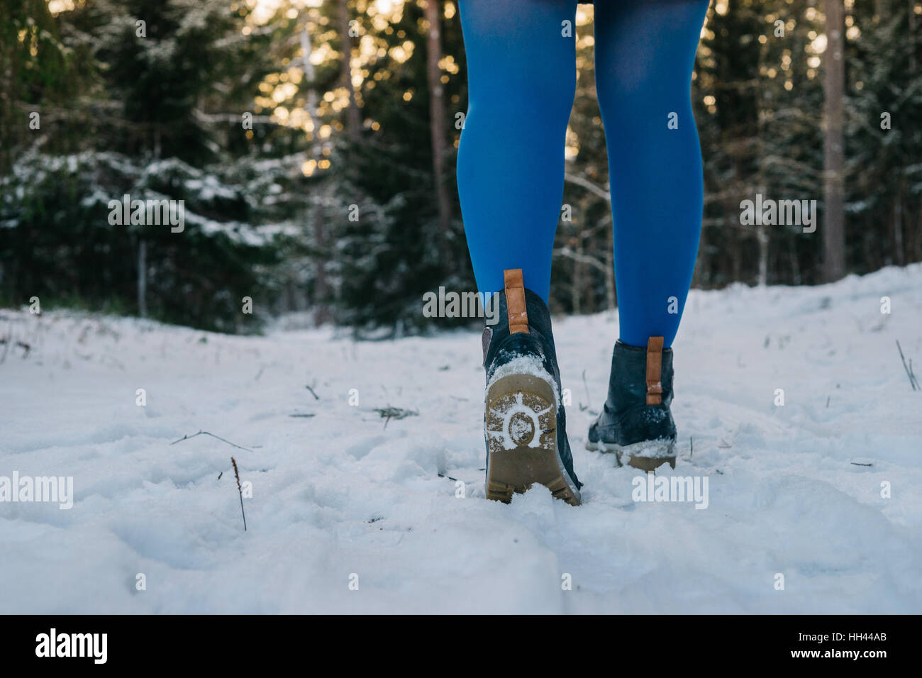 Weibliche Beine in trendigen Stiefeln und blaue Strumpfhose gegen verschneiten Wald. Hinten Sie Ansicht von vom Boden Stockfoto