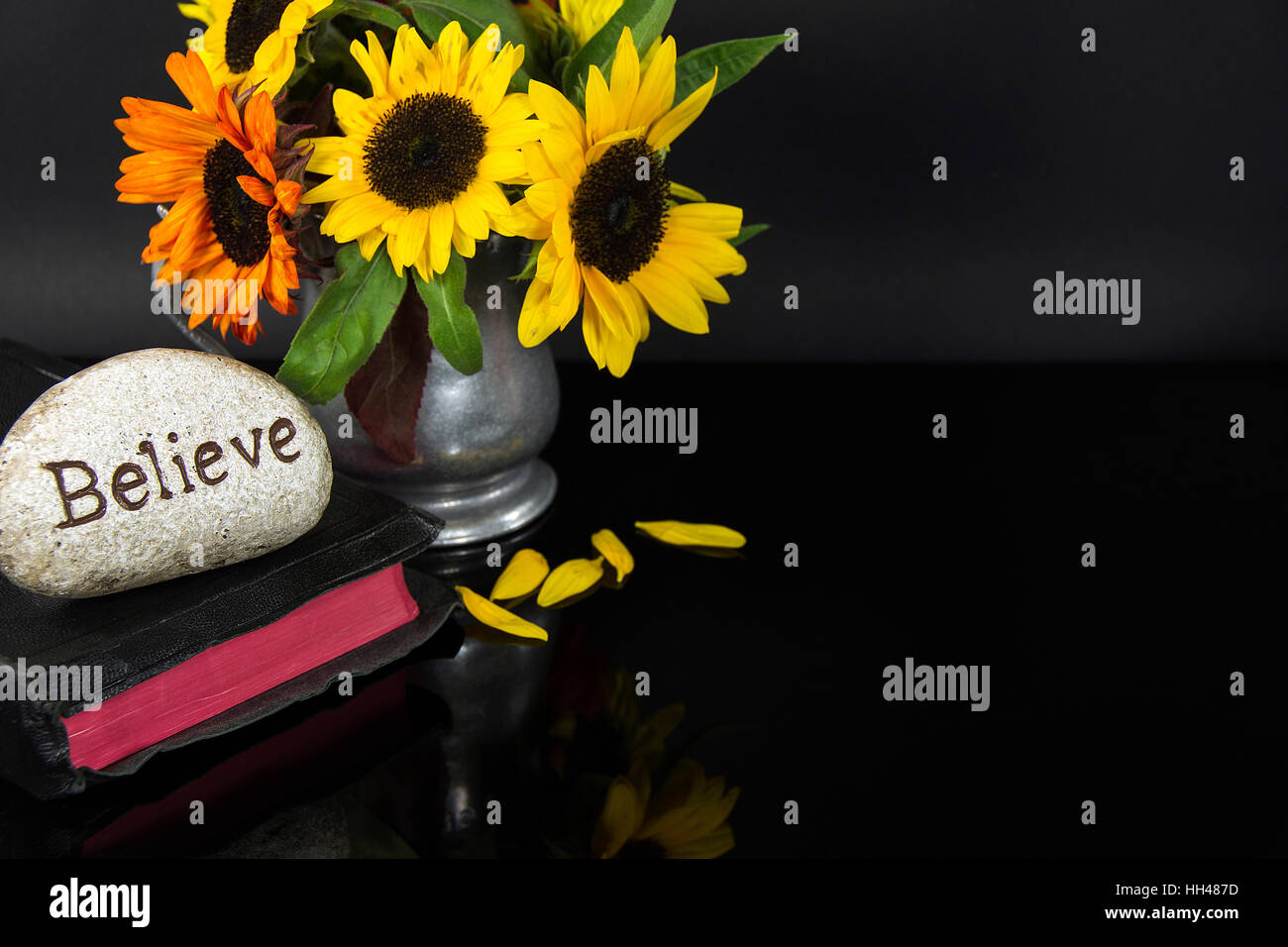 Wort zu glauben geschnitzten Stein auf schwarze Bibel mit Sonnenblumen Blumenstrauß Stockfoto