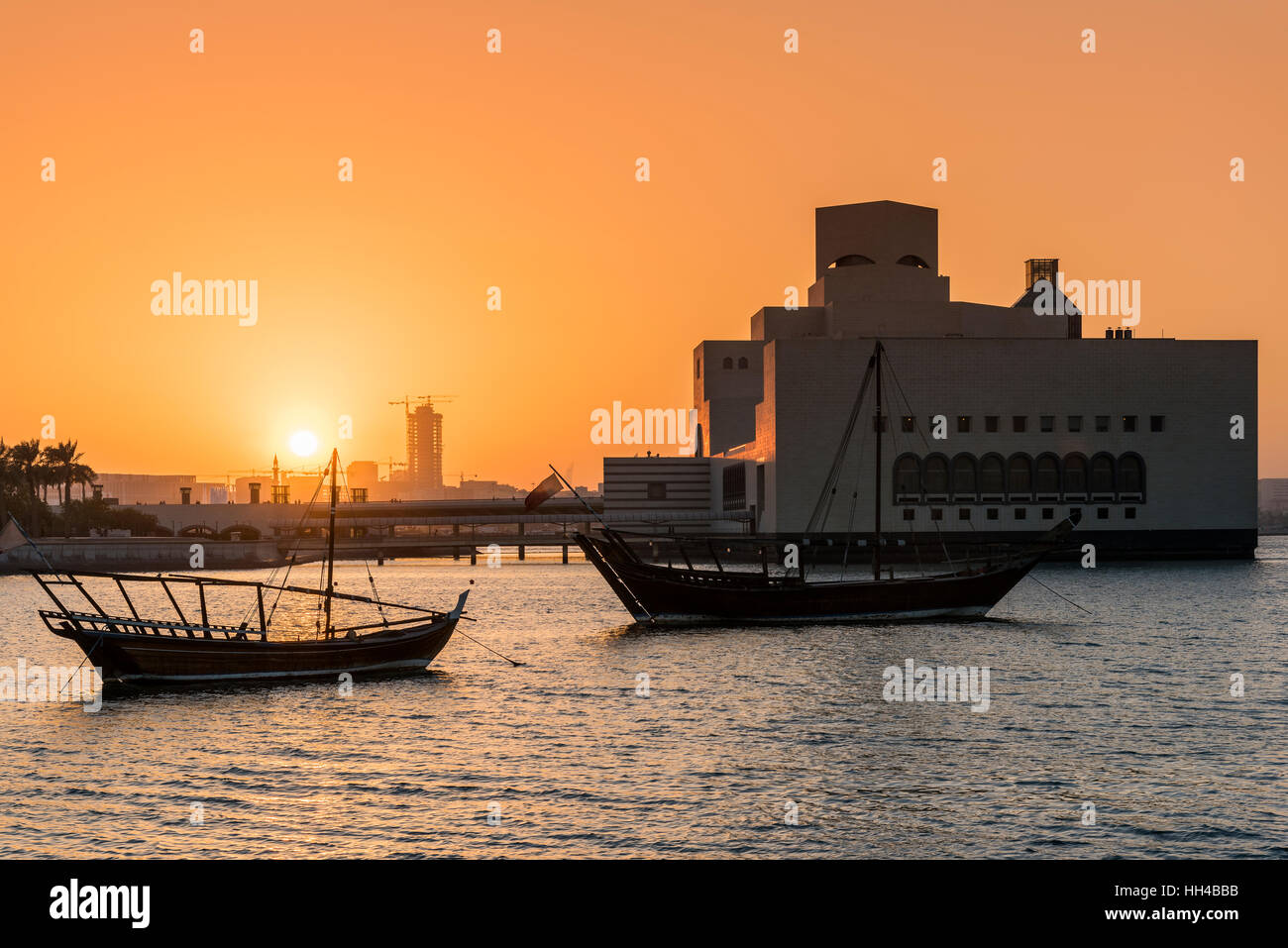 Blick auf den Sonnenuntergang über traditionelle Dhaus Boote mit Museum für islamische Kunst hinter, Doha, Katar Stockfoto