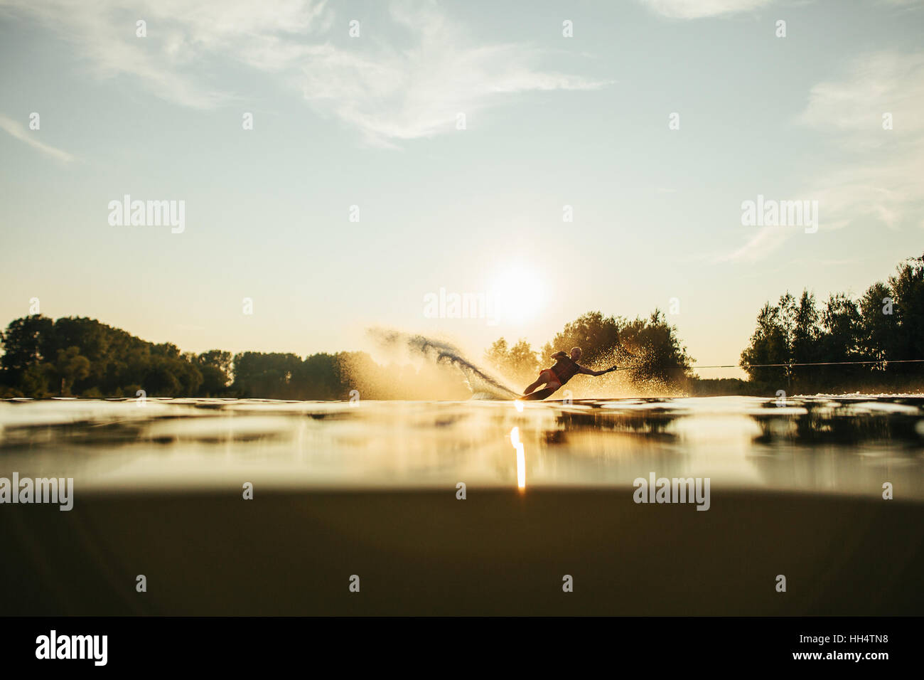 Niedrigen Winkel Schuss von Mann Wasserski bei Sonnenuntergang. Mann Wakeboarden an einem See. Stockfoto