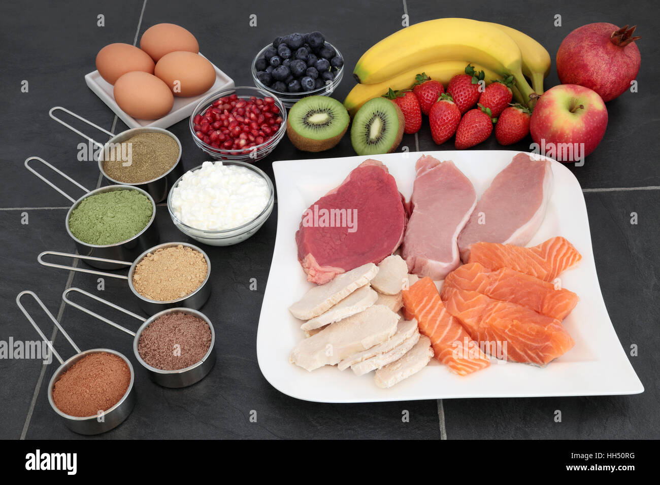 Bodybuilding Nahrung Ergänzung Pulver, proteinreichen mageres Fleisch und Lachs, Obst und Milchprodukte über Schiefer Hintergrund. Stockfoto