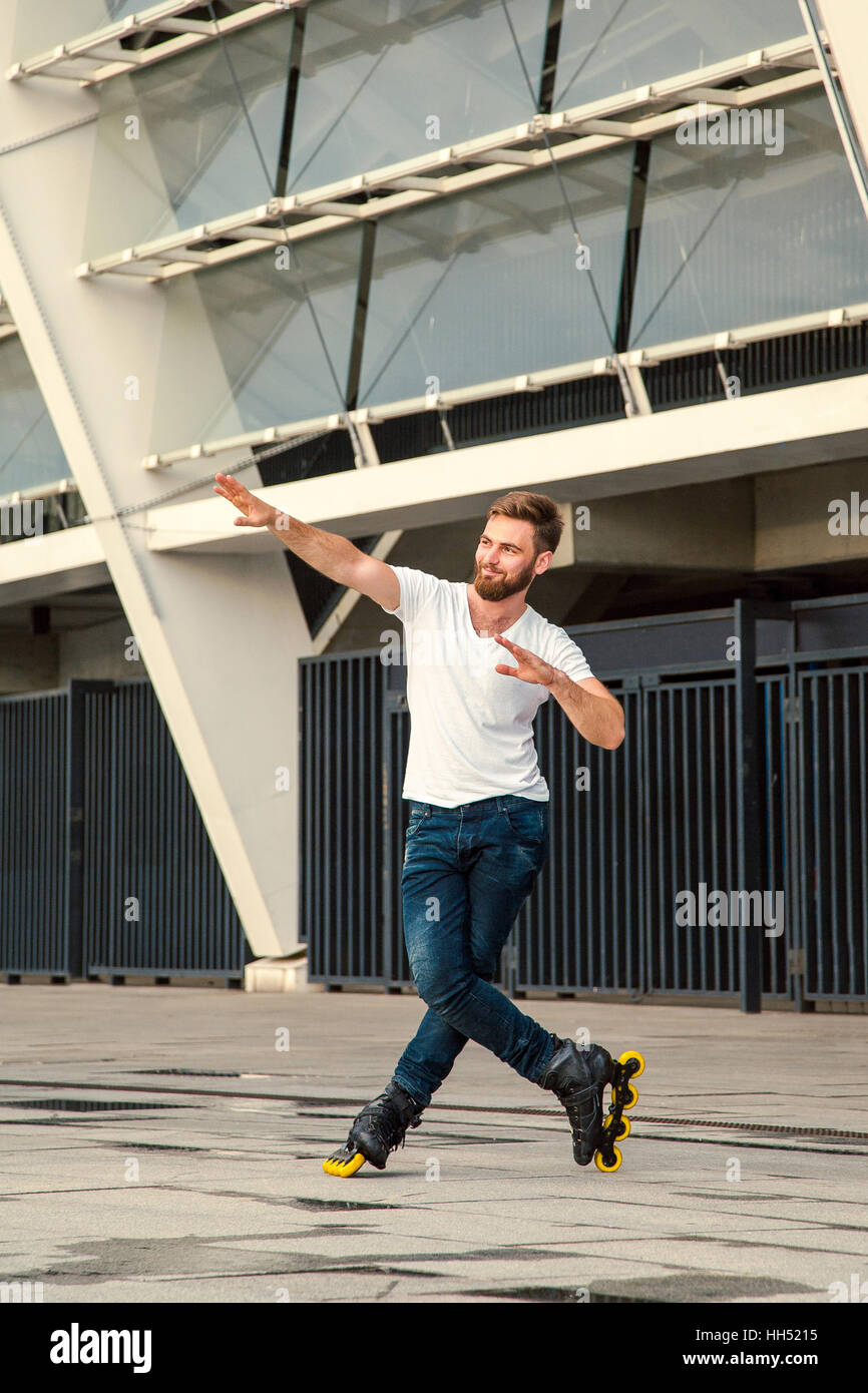 Bärtiger Mann auf Rollerblades stehen im Hintergrund Gebäude. Jungen passen Mann mit weißen T-shirts und Jeans auf Rollschuhen fahren Stockfoto