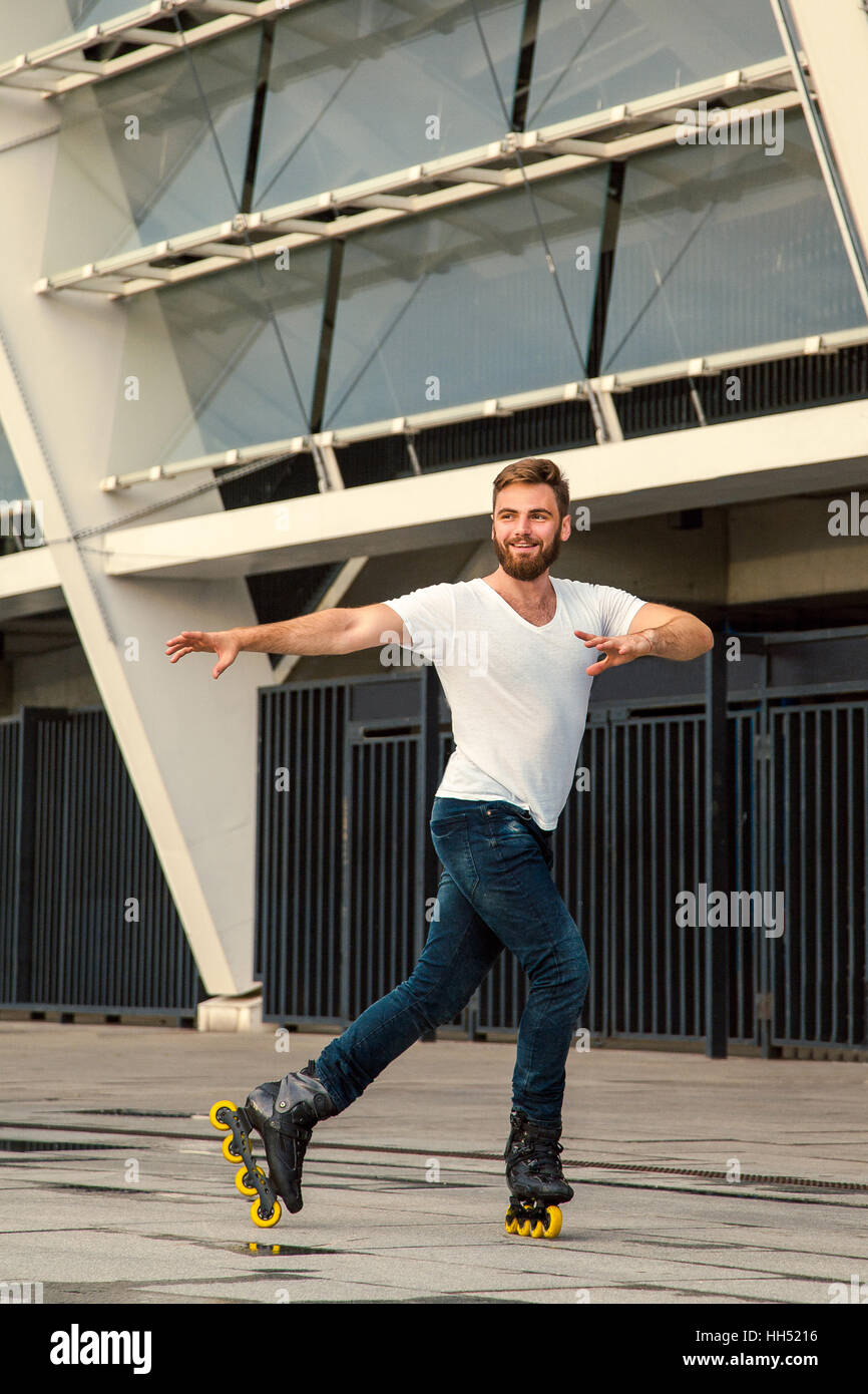 Bärtiger Mann auf Rollerblades stehen im Hintergrund Gebäude. Jungen passen Mann mit weißen T-shirts und Jeans auf Rollschuhen fahren Stockfoto