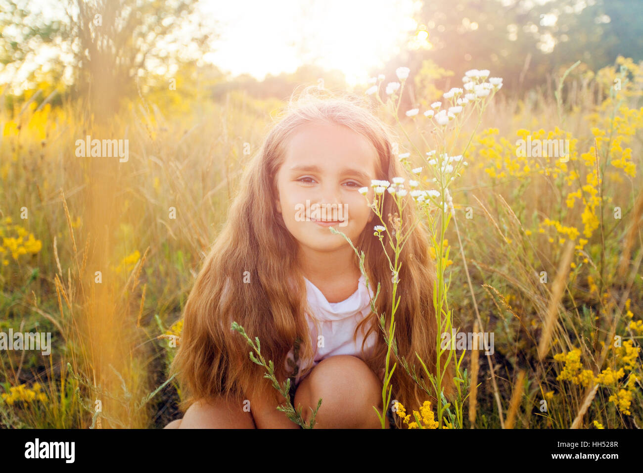 Schöne kleine Mädchen mit langen Haaren und Lächeln im Sommer im sunset Park. posieren und Blick in die Kamera und lächelnd. Stockfoto