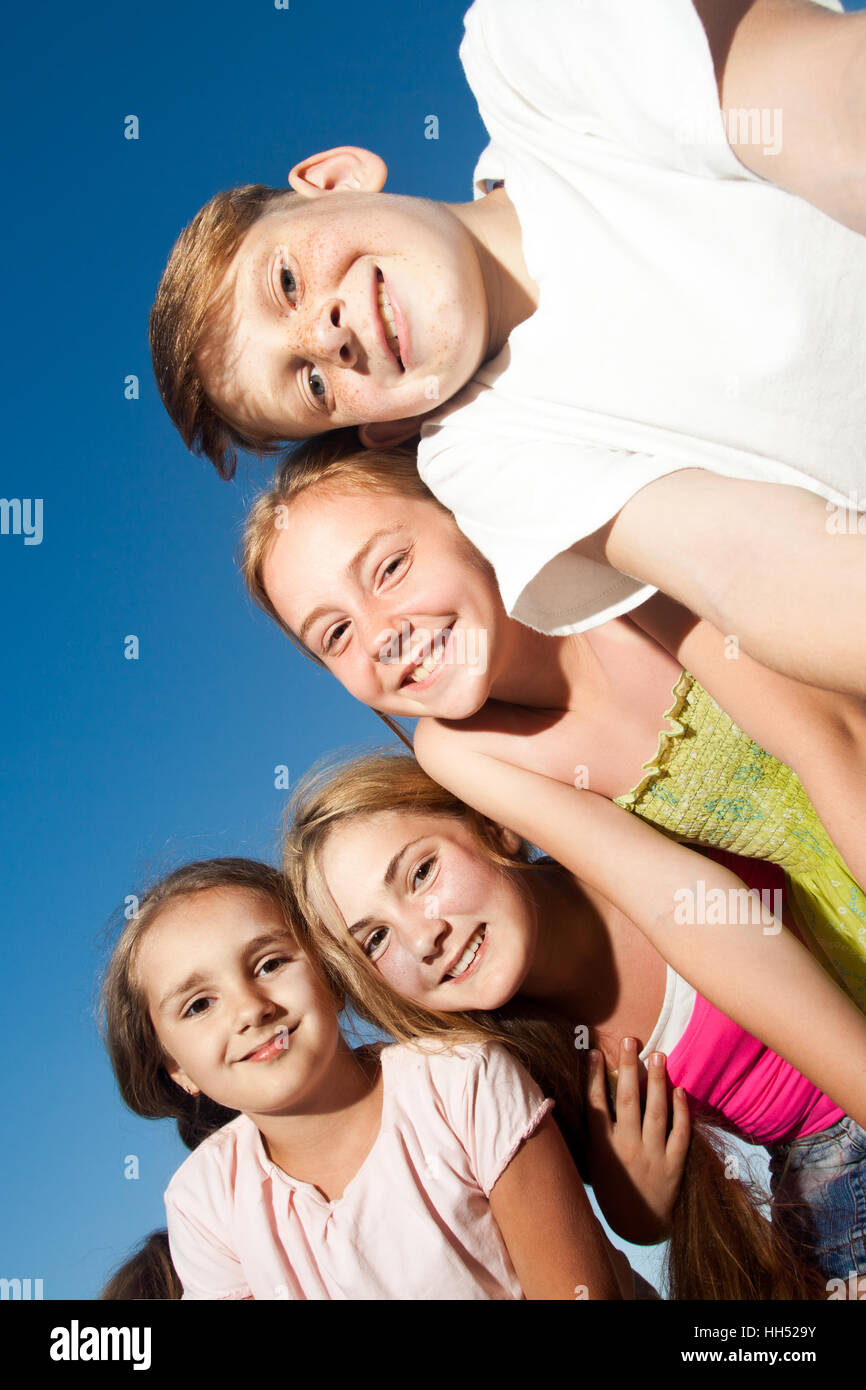 vier schöne glückliche Kinder Blick in die Kamera von oben in den sonnigen Sommertag und blauer Himmel. Blick in die Kamera mit lustigem Gesicht Stockfoto