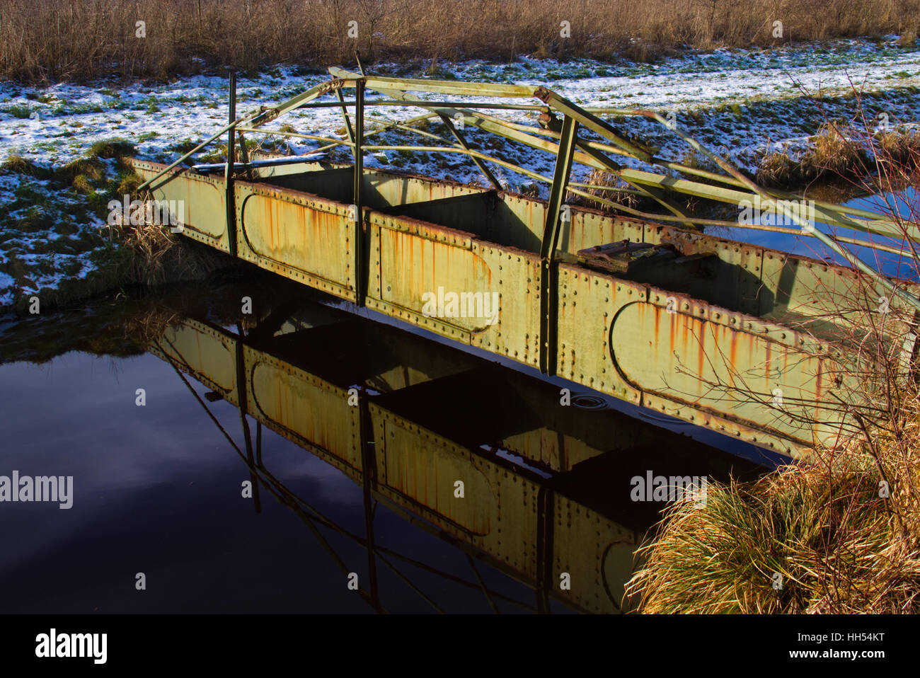 Alte rostige Steg spiegelt sich im Wasser eines Kanals, Handläufe von Metallermüdung gebogen Stockfoto