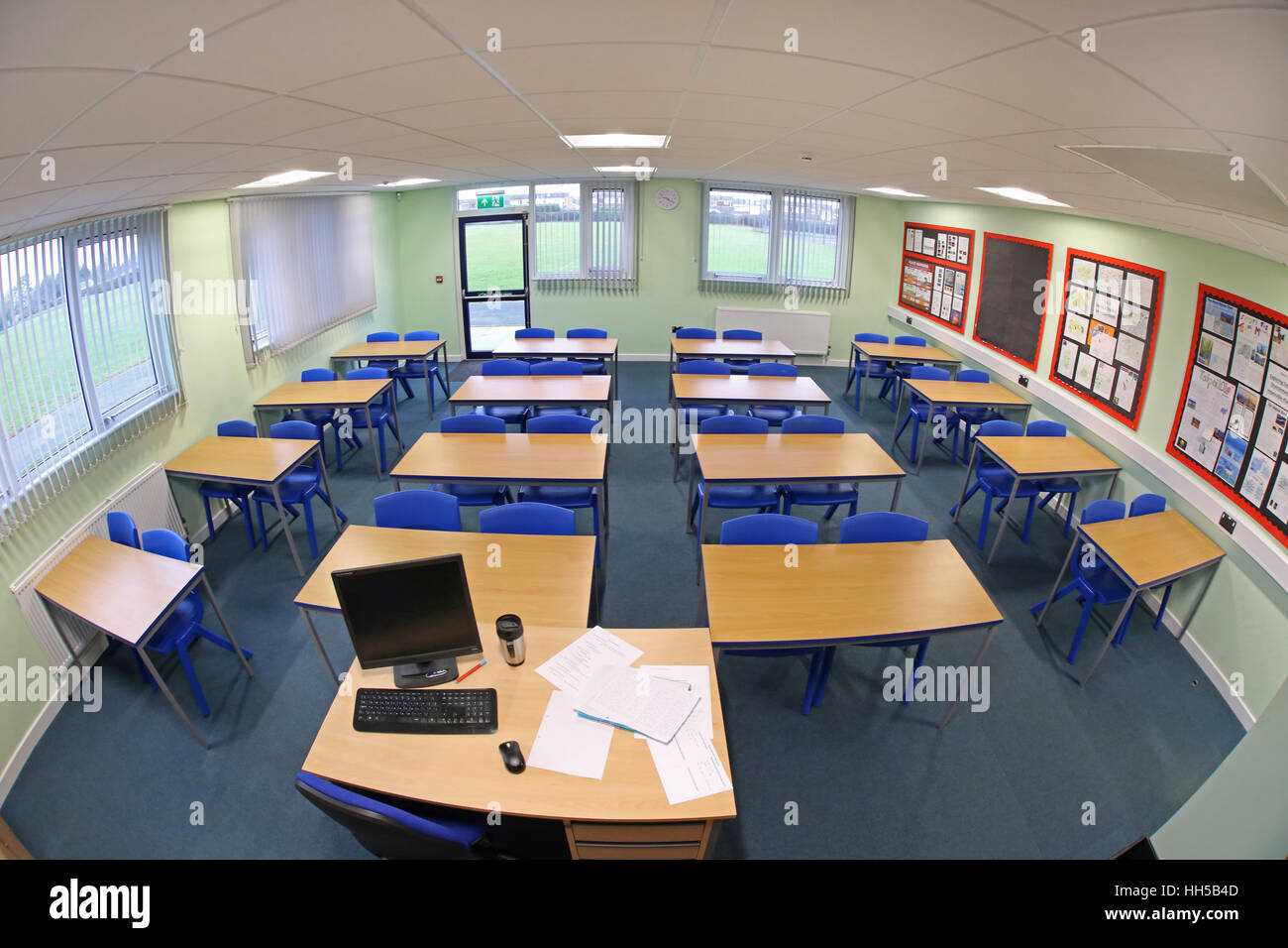 Weitwinkelansicht eines neu erbauten Schulklasseraums mit Schreibtischen und Stühlen in traditioneller Anordnung, gegenüber dem Lehrerschreibtisch. Leer, keine Pupillen. Stockfoto