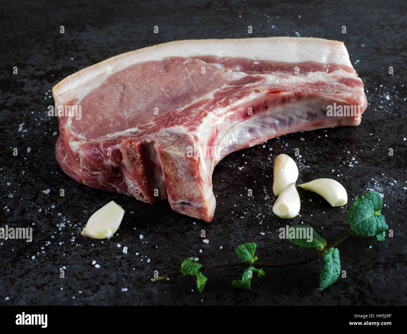 Rohes Schweinefleisch Chop, Knoblauch, Minze und Salz auf schwarzem Stein Stockfoto