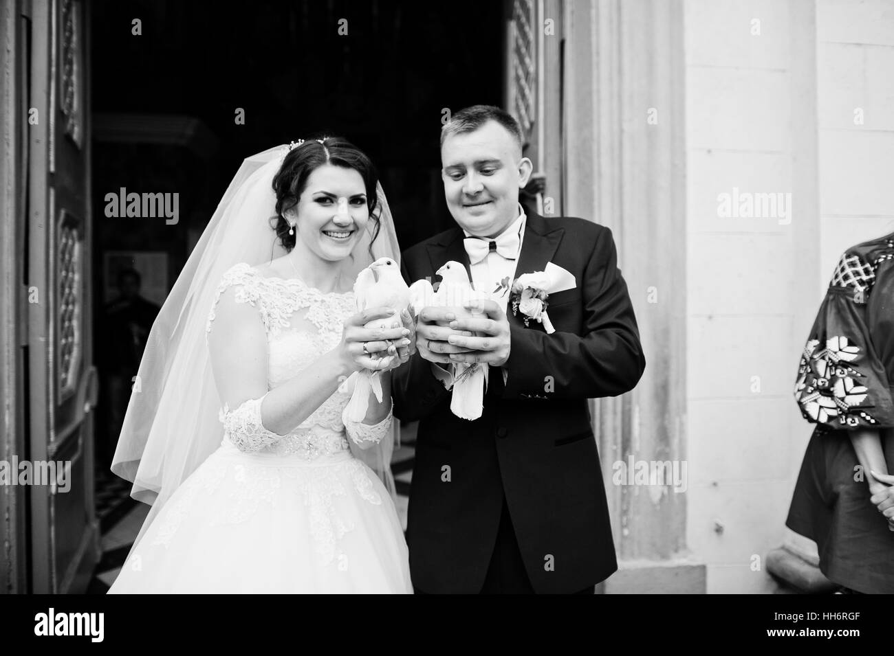 Glücklich lächelte Brautpaar mit Tauben auf Händen nach der Hochzeit Registrierung auf Kirche. Schwarz / weiß Foto Stockfoto