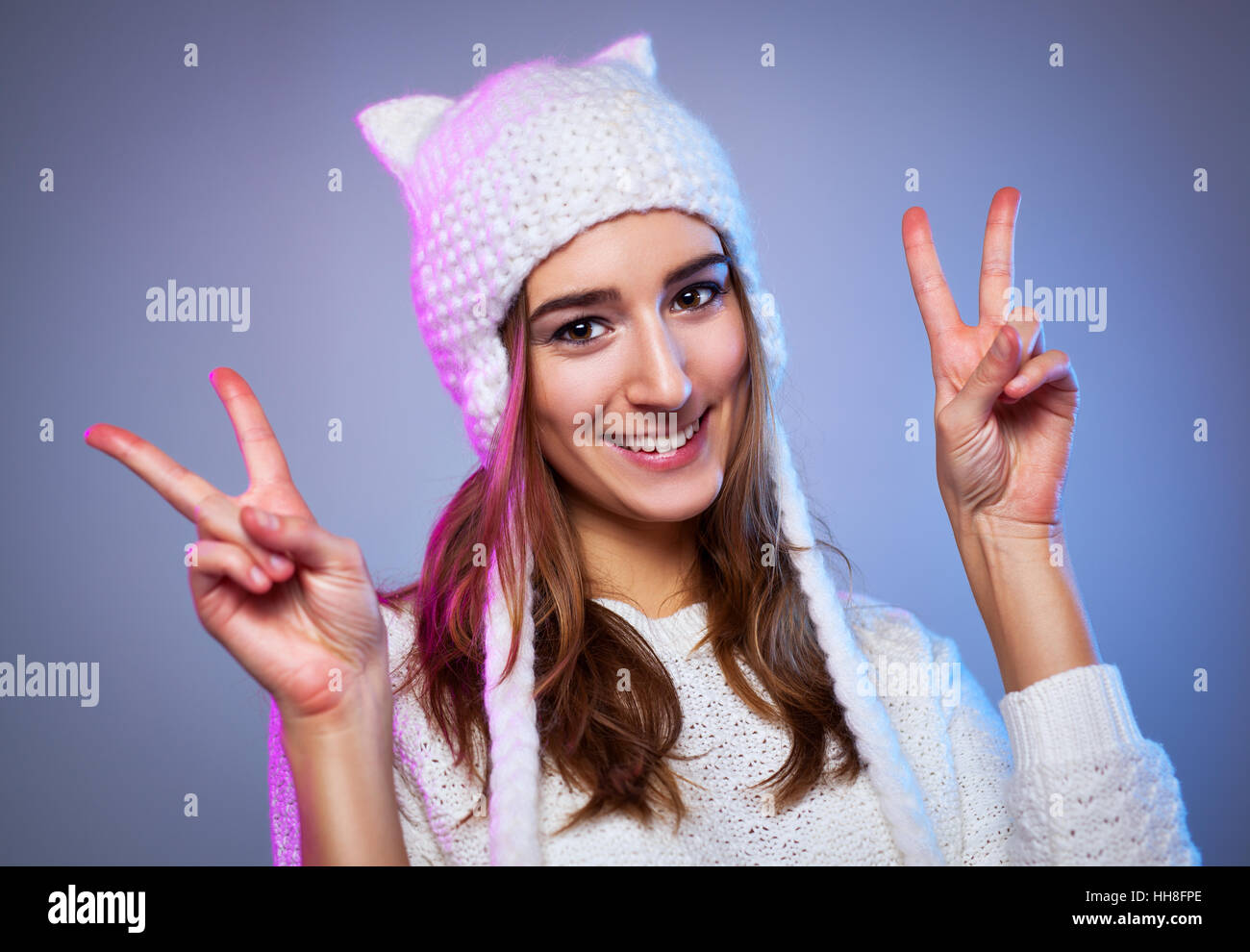 Junge glücklich lächelnde Frau zeigt Sieg zu unterzeichnen. Warme Winterkleidung weiß. Stockfoto