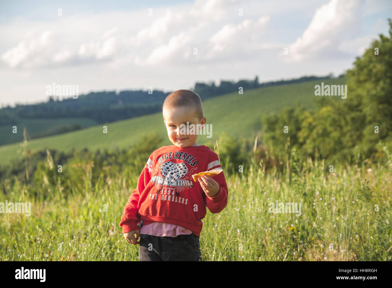 Lächelnde junge Kind in rote Bluse einen Muffin zu essen, auf der grünen Wiese Stockfoto