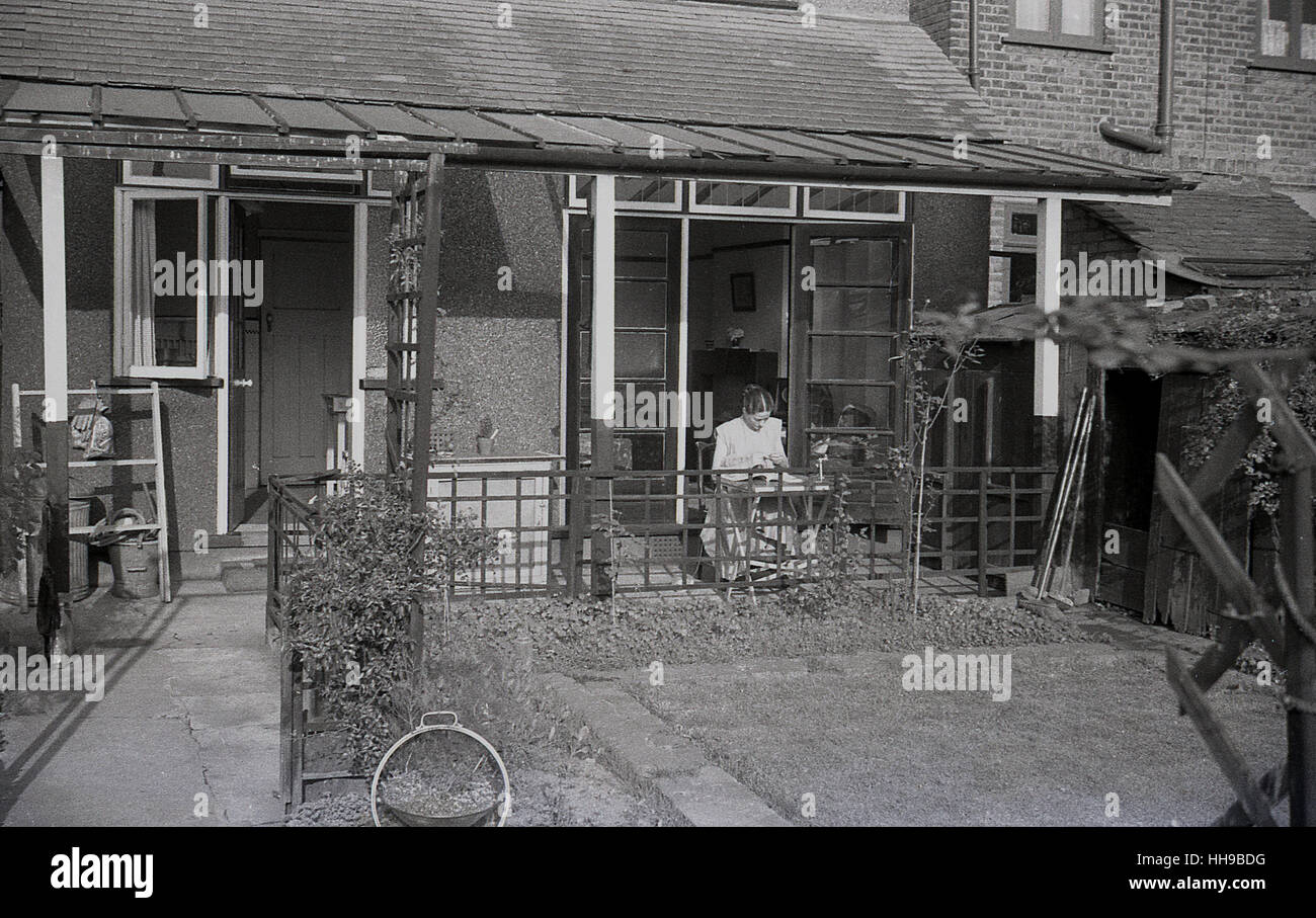 Öffnen Sie 1930er-Jahren, historische, Dame ein Buch sitzen unter einem Glas überdacht, endete Terrasse oder Veranda auf der Rückseite eines Hauses. Stockfoto