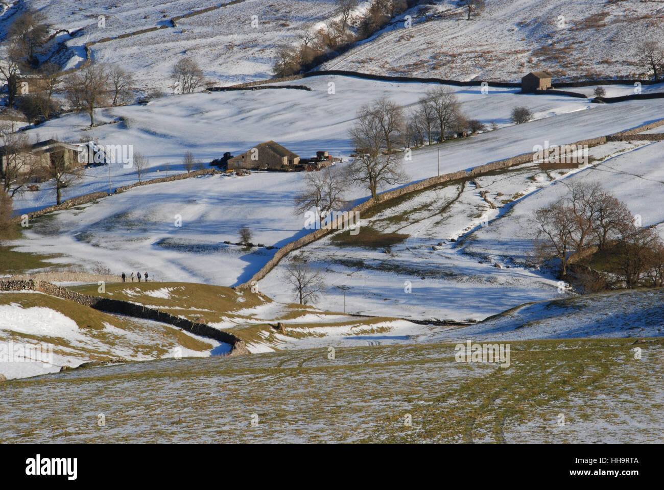 Vier Wanderer auf einem klaren Wintertag wandern über die Bauernlandschaft in Yorkshire mit Schnee auf dem Boden Stockfoto