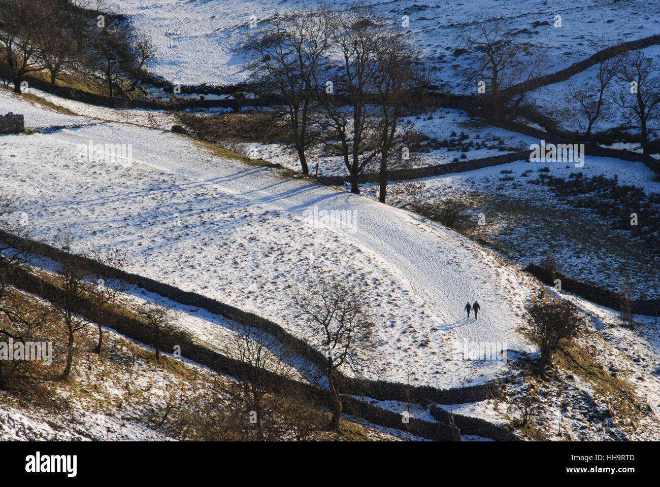 Zwei Figuren, die durch eine winterliche und verschneite Landschaft spazieren, die von einer tief liegenden Nachmittagsonne in der Nähe von Malham in Yorkshire beleuchtet und hervorgehoben wird Stockfoto