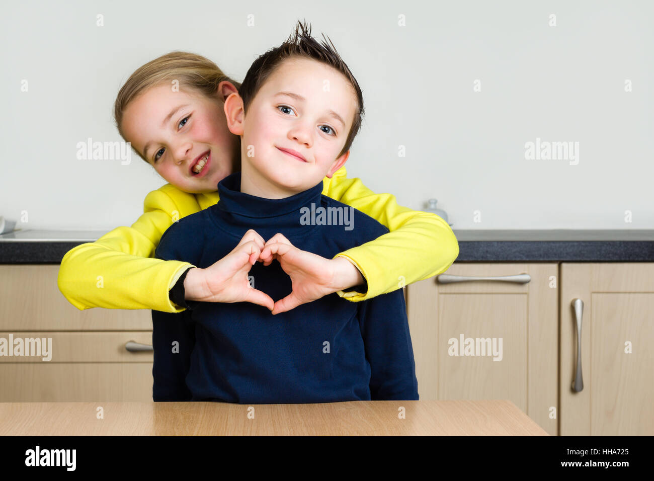 Kleine Kinder (Geschwister Junge und Mädchen) Hug und Mädchen formen Herzen mit Händen zu Hause in der Küche Stockfoto