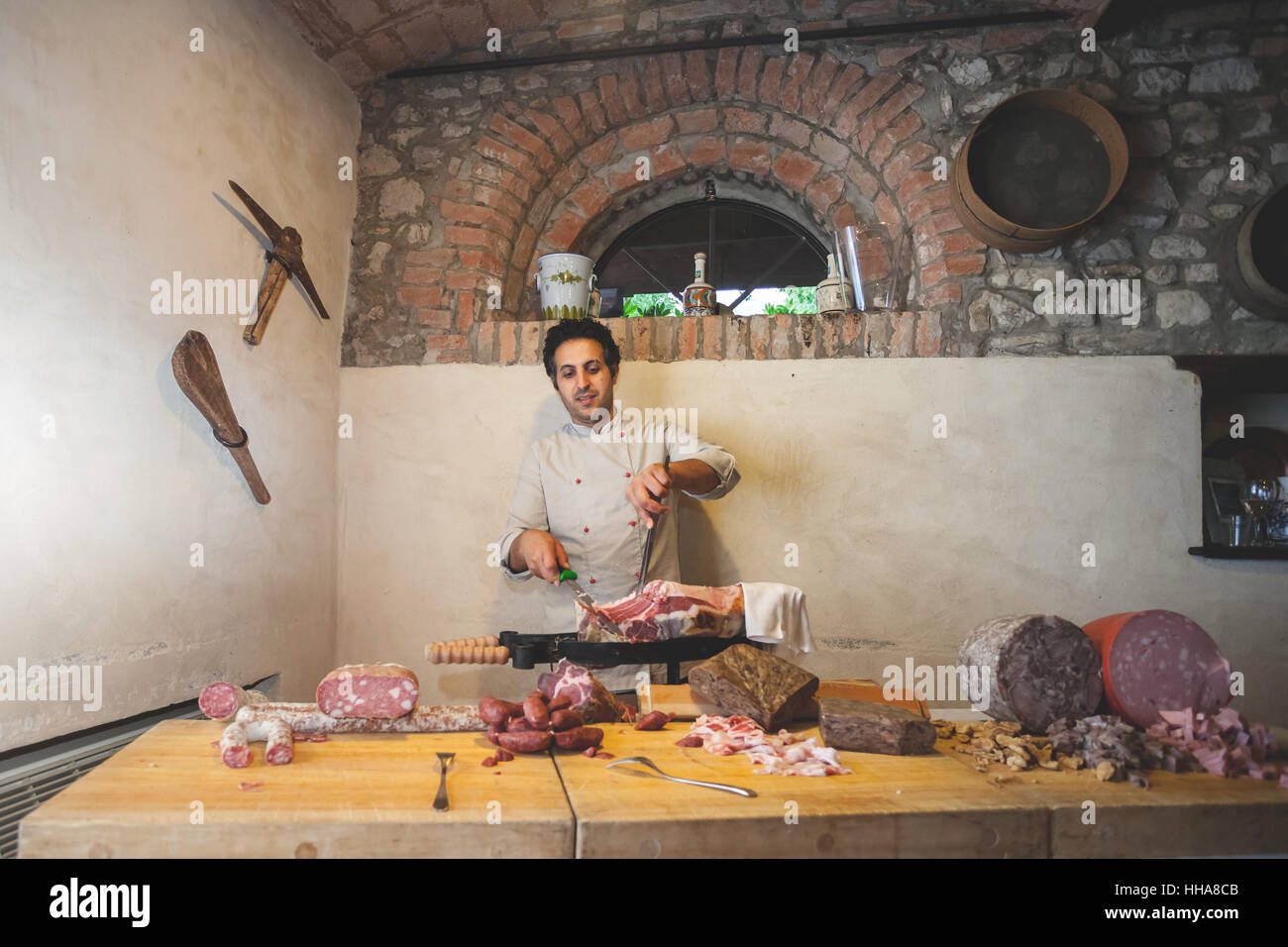 Italienischen Koch vor einem Tisch voller Fleischwaren, Schinken aus einem Stück Schweinefleisch schneiden Stockfoto