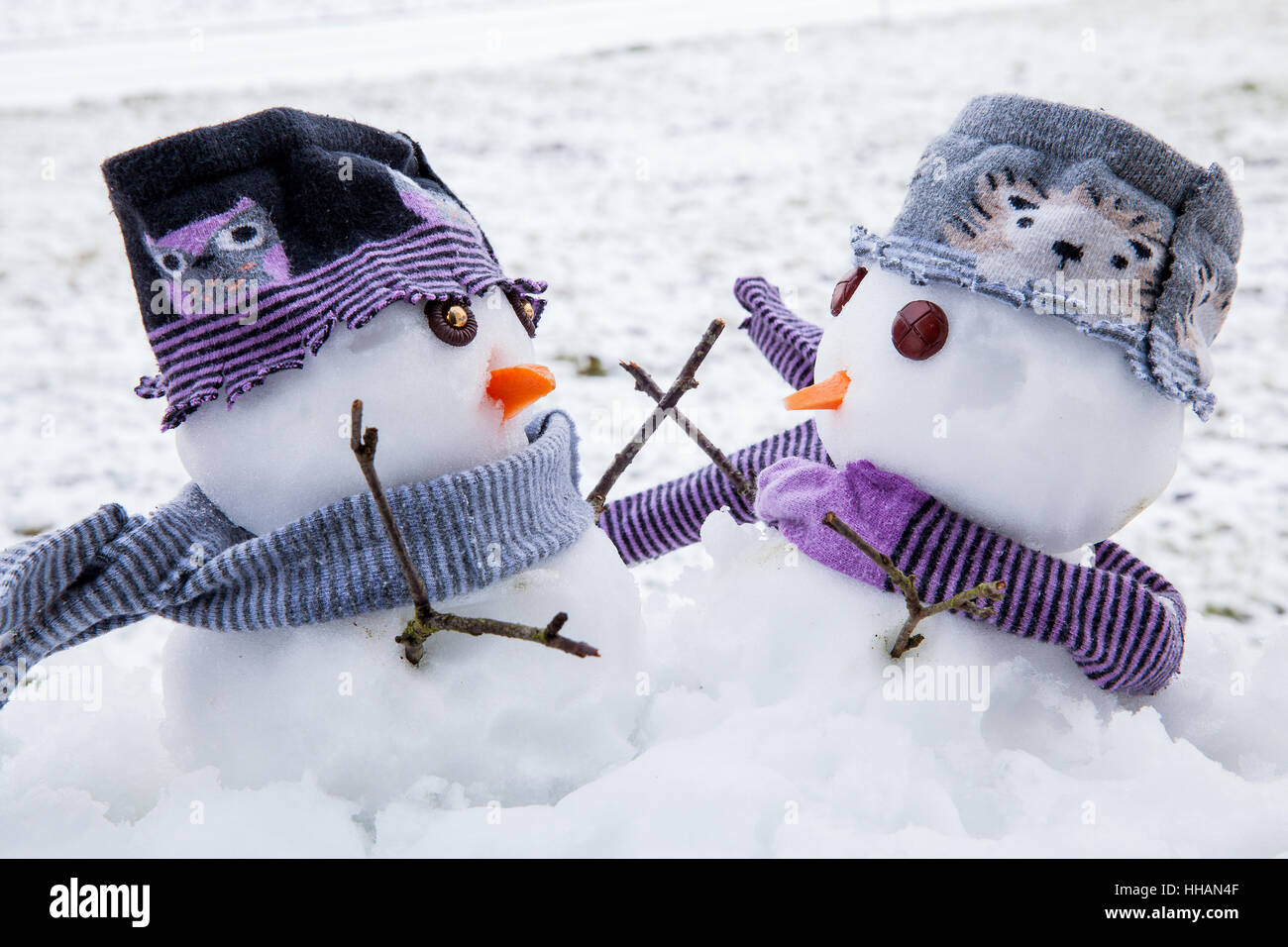 Zwei niedliche Schneemänner gekleidet für den Winter in Schals und Mützen umarmen einander als lange verlorene Freunde. Winterlandschaft mit Schnee. Stockfoto