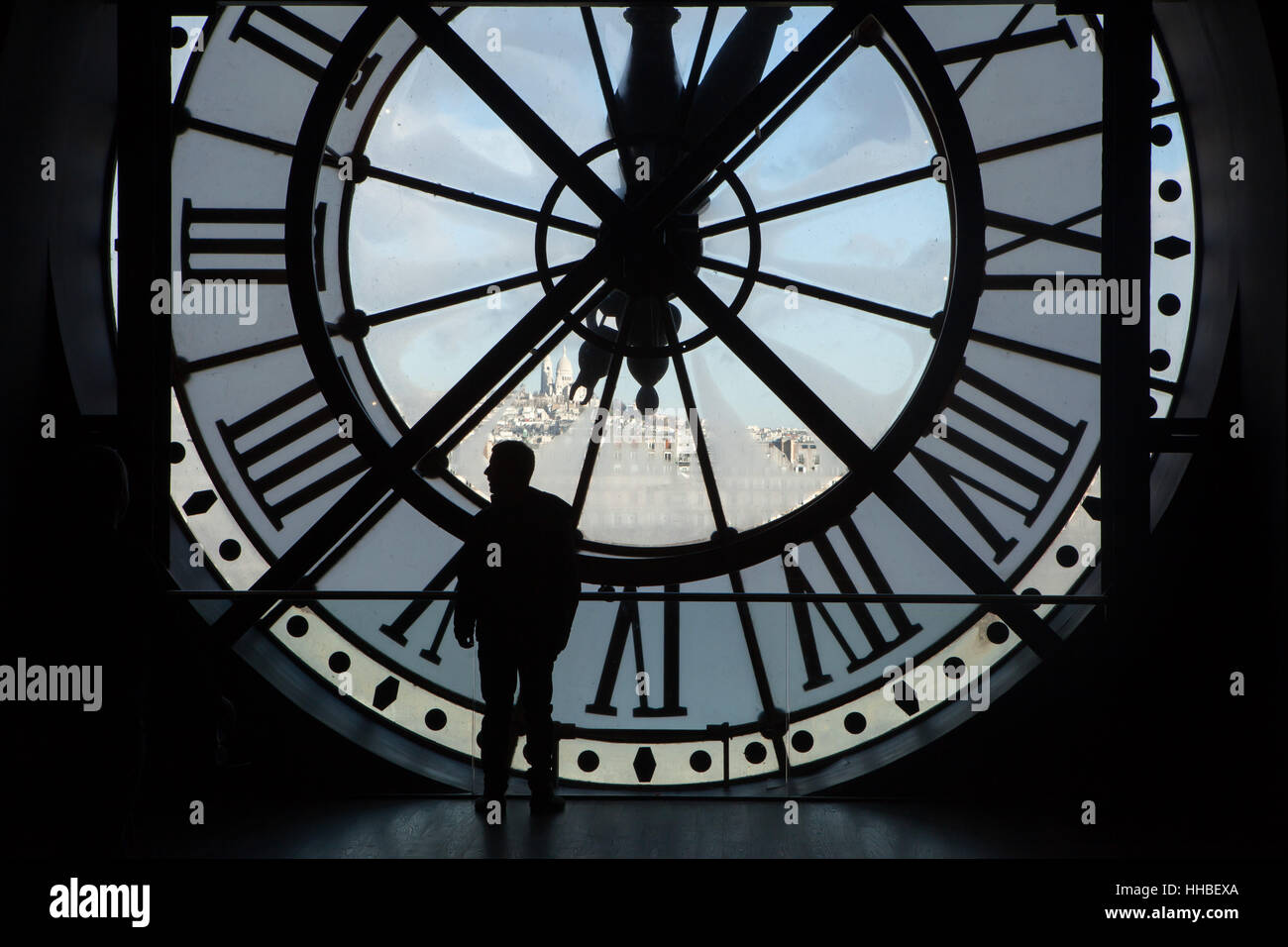 Besucher sieht, Gedanken, die das große Glas Uhr im Musée d ' Orsay in Paris, Frankreich. Basilika Sacré-Coeur auf dem Montmartre (Basilique du Sacré-Coeur de Montmartre) ist im Hintergrund zu sehen. Stockfoto
