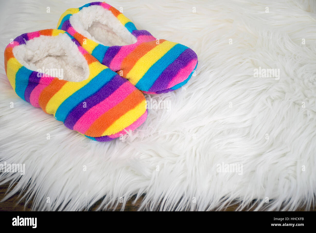 Regenbogen-Pantoffeln auf weißem Fell Teppich Stockfoto