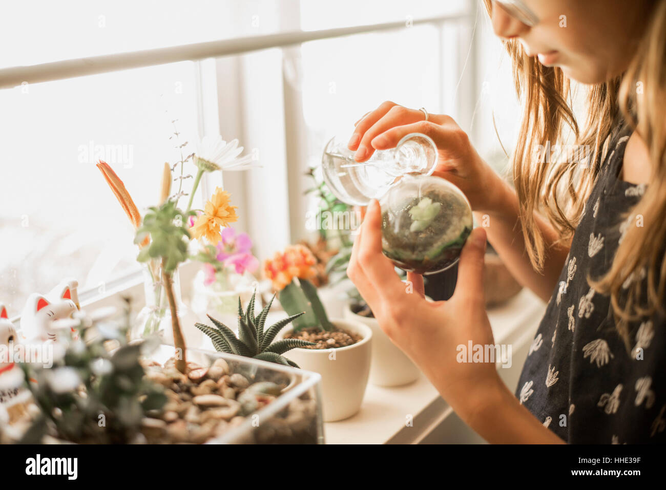 Mädchen tendenziell Pflanzen auf einer sonnigen Fensterbank. Stockfoto