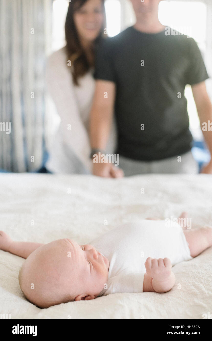 Zwei Eltern Hand in Hand, ein junges Baby auf einem Bett liegend überragt. Stockfoto