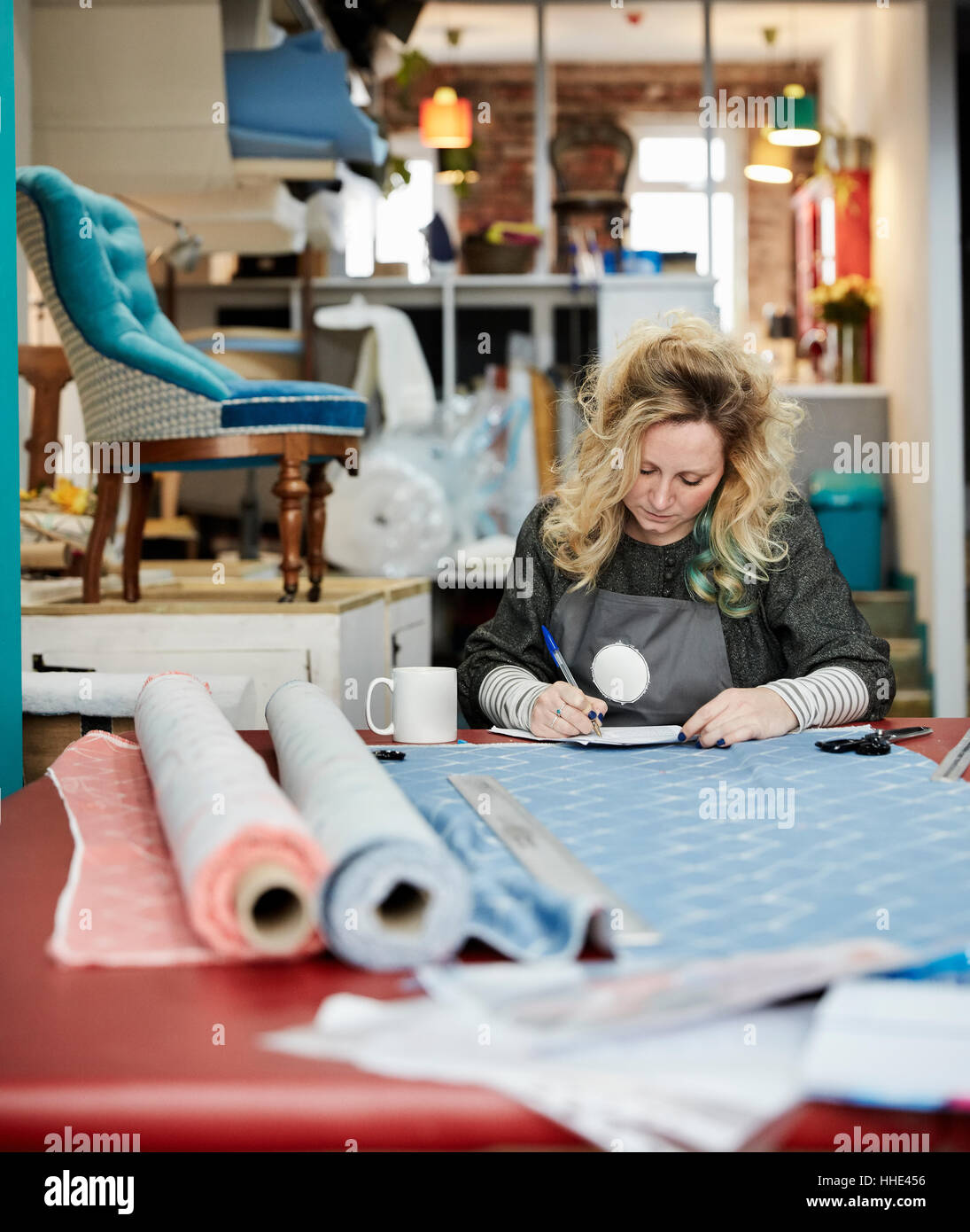 Eine Frau vorbereiten, Messen und schneiden Bezugsstoff auf einer Werkbank. Stockfoto
