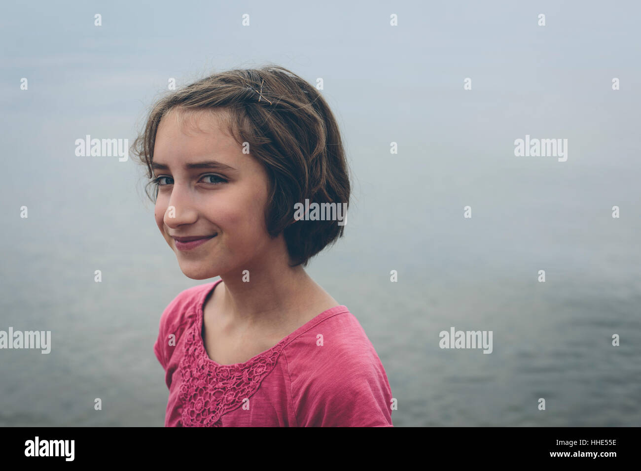 Porträt der Glückliche elf Jahre alte Mädchen im Freien in einem rosafarbenen Hemd seitwärts lächelte Kamera. Stockfoto