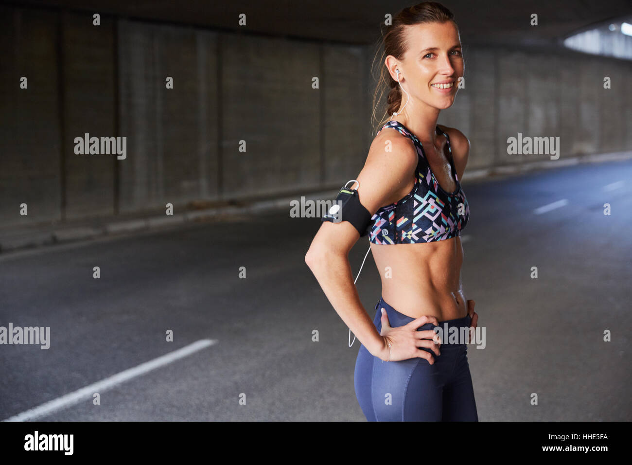 Porträt lächelnd passen weibliche Läufer in Sport-BH mit Armband für MP3-Player und Kopfhörer in städtischen tunnel Stockfoto