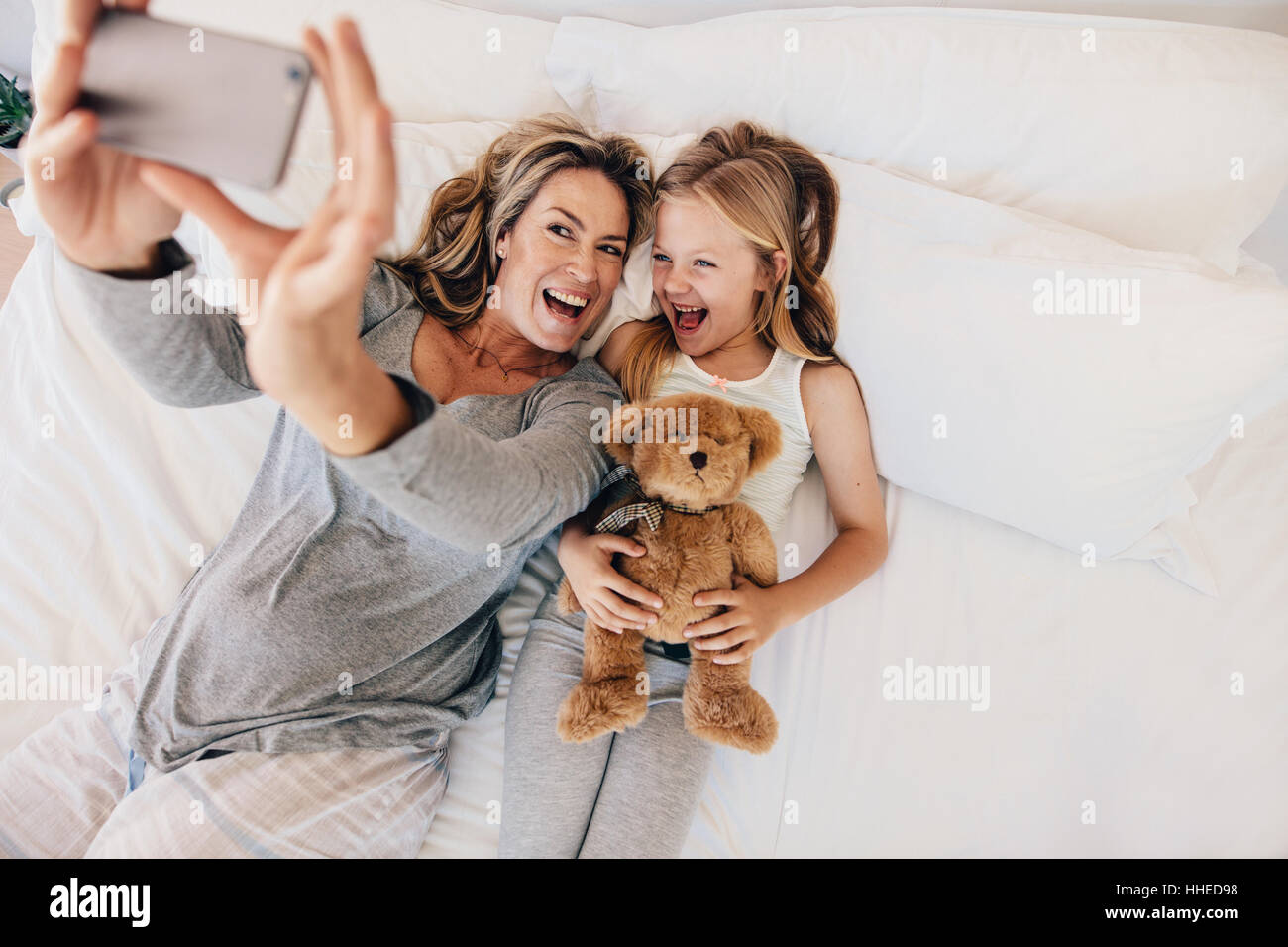 Glückliche junge Mutter nehmen Selfie mit ihrer Tochter. Junge Familien nehmen Selfie auf Bett zu Hause. Stockfoto
