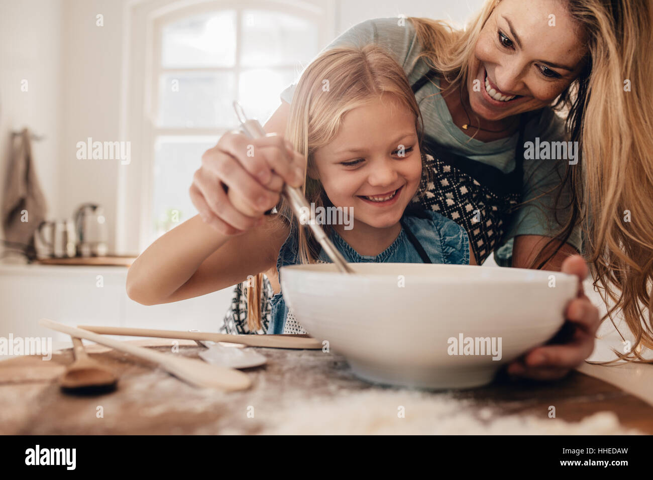 Junge Familie kochen in der Küche. Fröhliches junges Mädchen mit ihrer Mutter, der Teig in der Schüssel mischen. Stockfoto