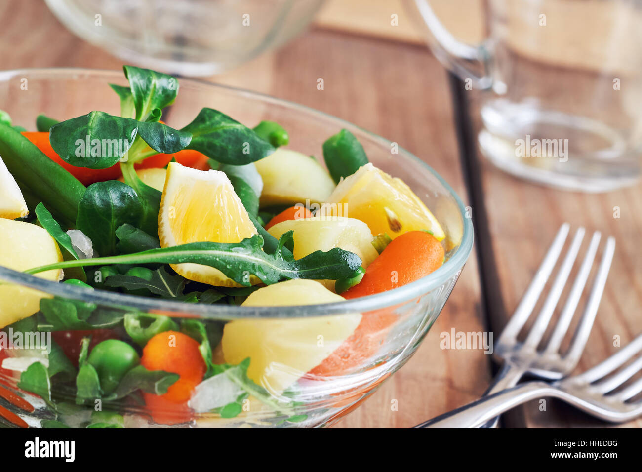 Salat mit Baby-Karotten, Erbsen, Zwiebeln und Kartoffeln in Glasschüssel auf hölzernen Hintergrund Stockfoto