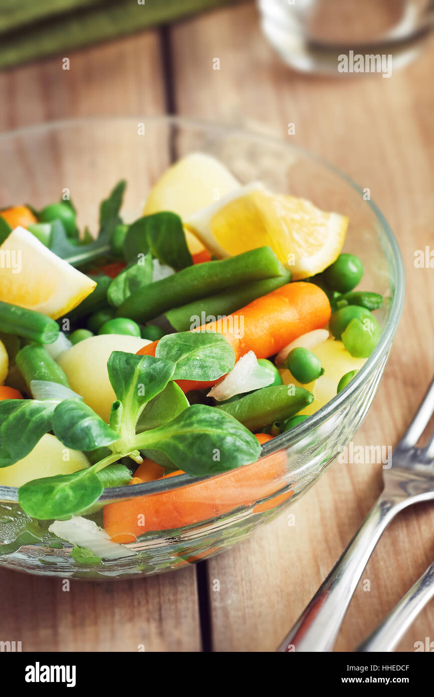 Salat mit Baby-Karotten, Erbsen, Zwiebeln und Kartoffeln in Glasschüssel auf hölzernen Hintergrund Stockfoto