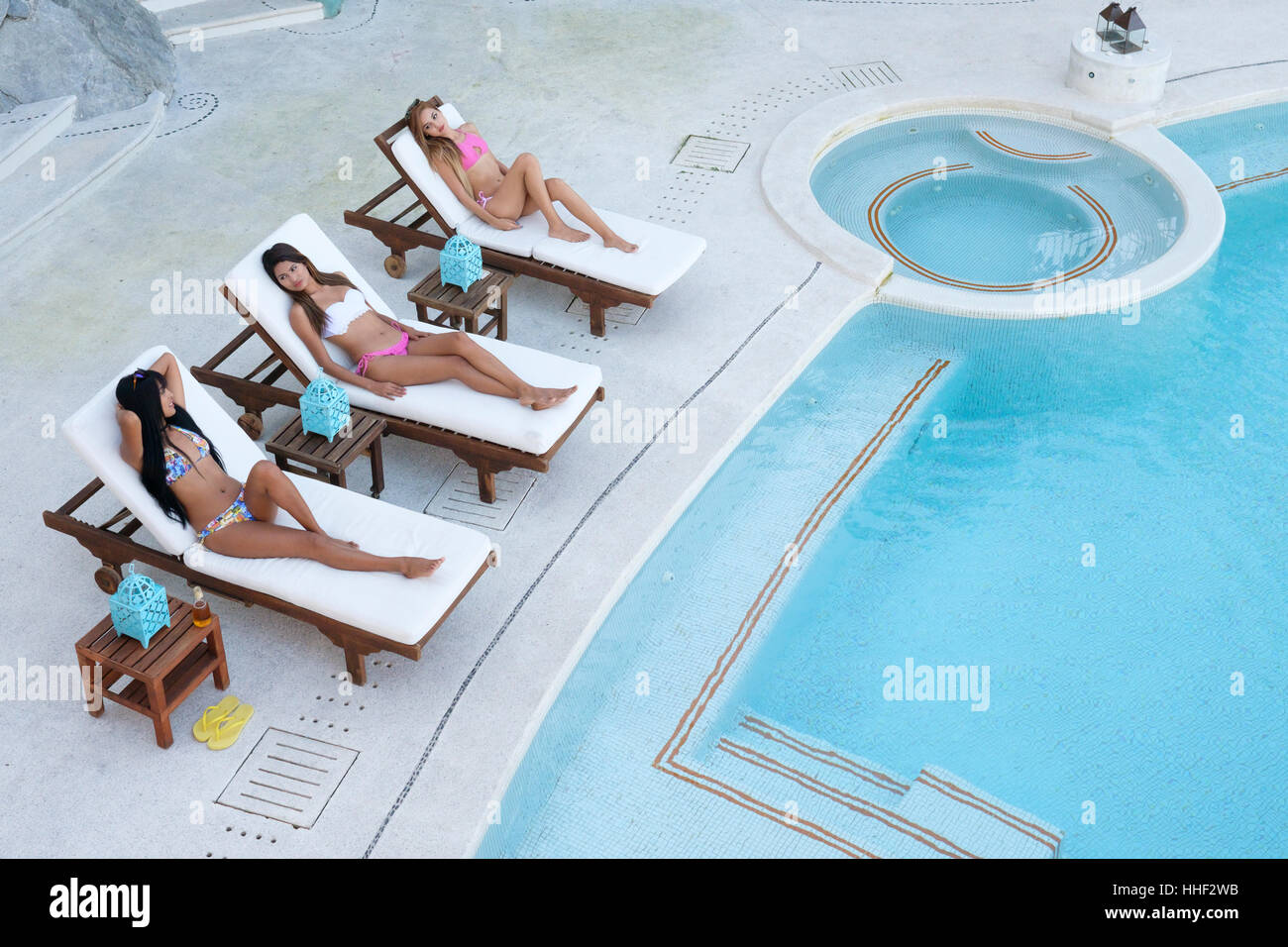 Drei junge attraktive hispanischen Frauen mit Liegestühlen für die Bräunung neben Schwimmbad Stockfoto