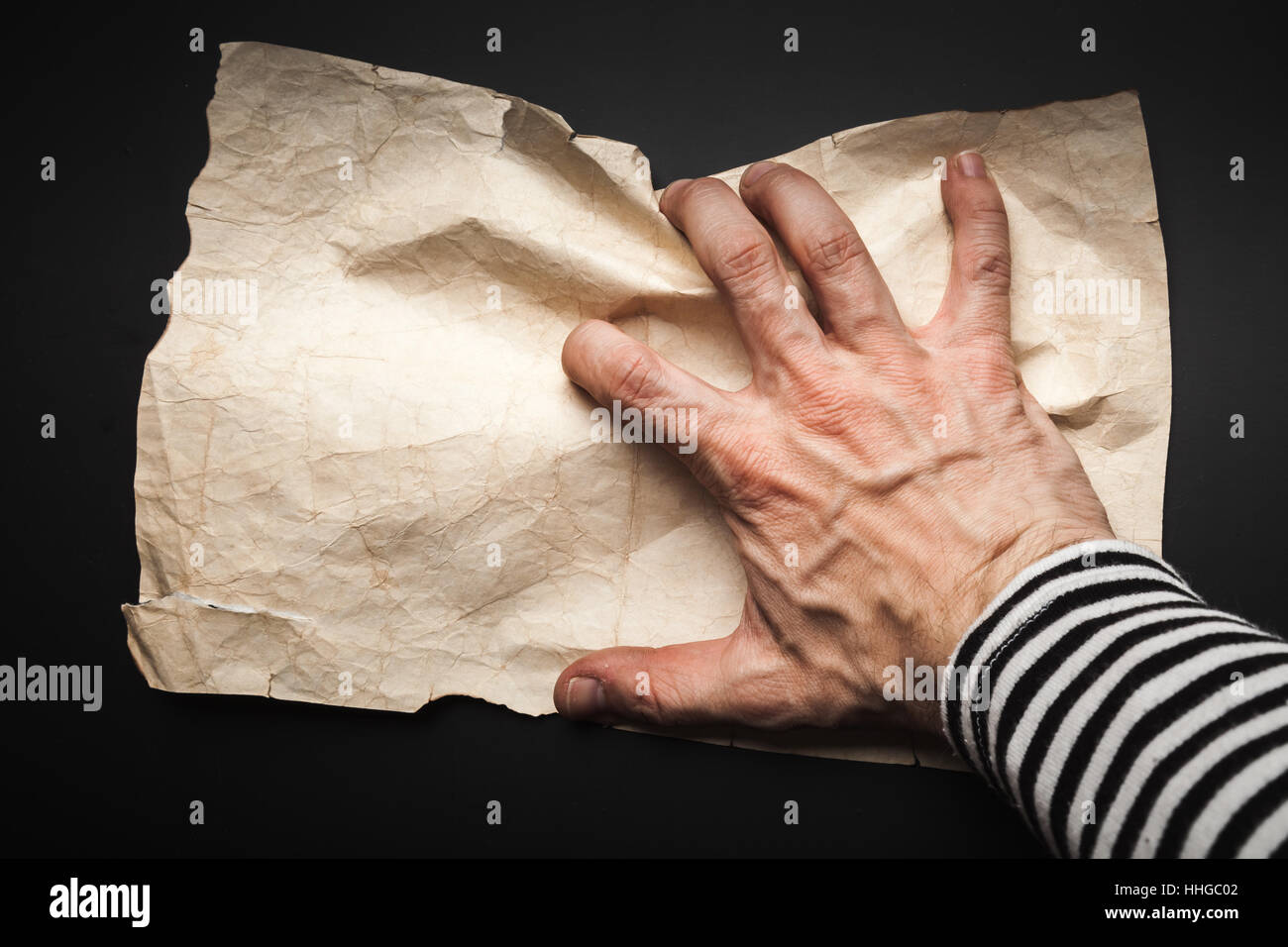 Starke Seemann Hand Fang leeren alten zerknittertes Papierblatt auf schwarzem Hintergrund, Piraten-Karte-Konzept Stockfoto