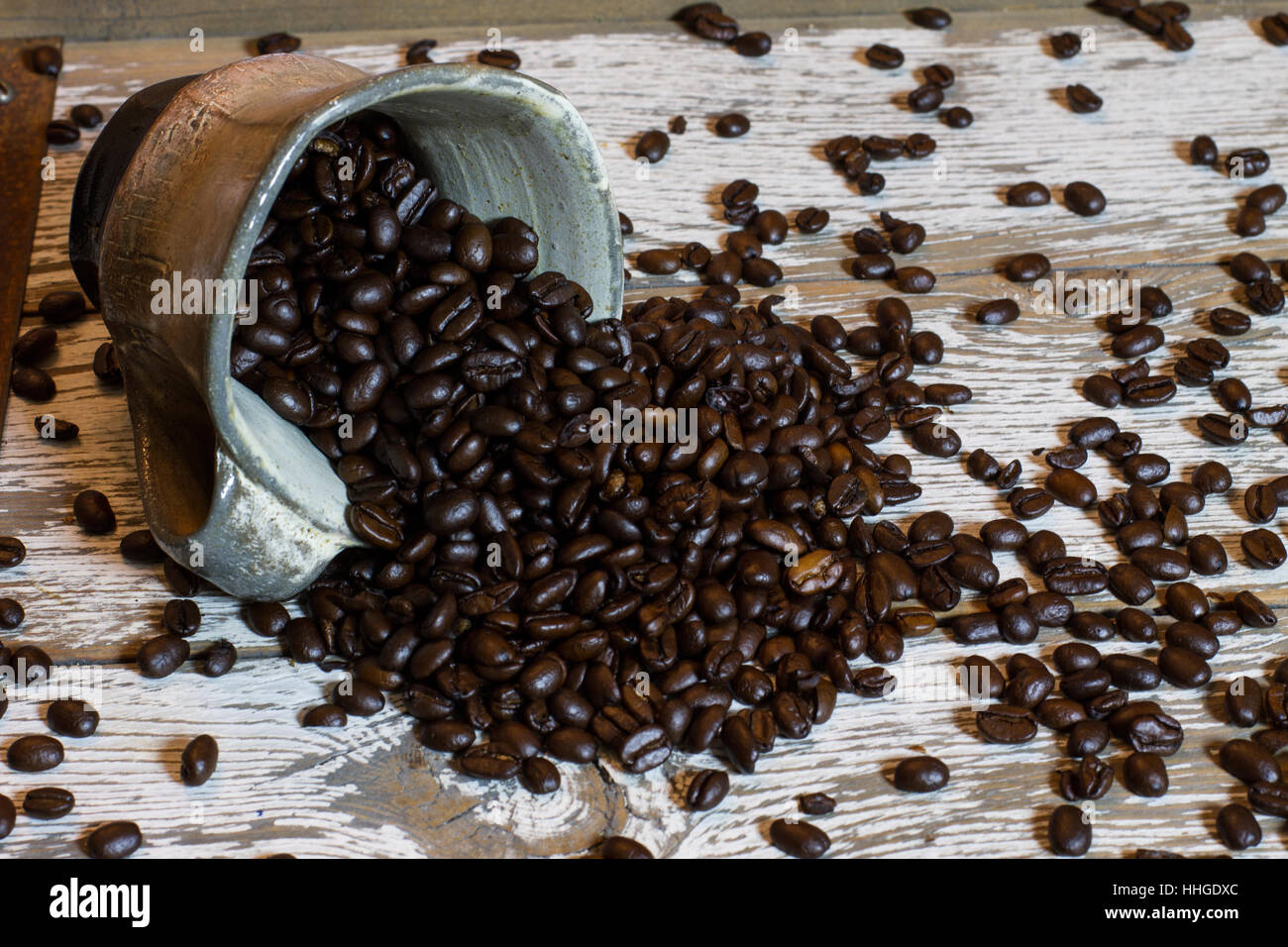 Kaffeebohnen aus eine schöne Tasse auf einem rustikalen Tisch verschütten. Stockfoto