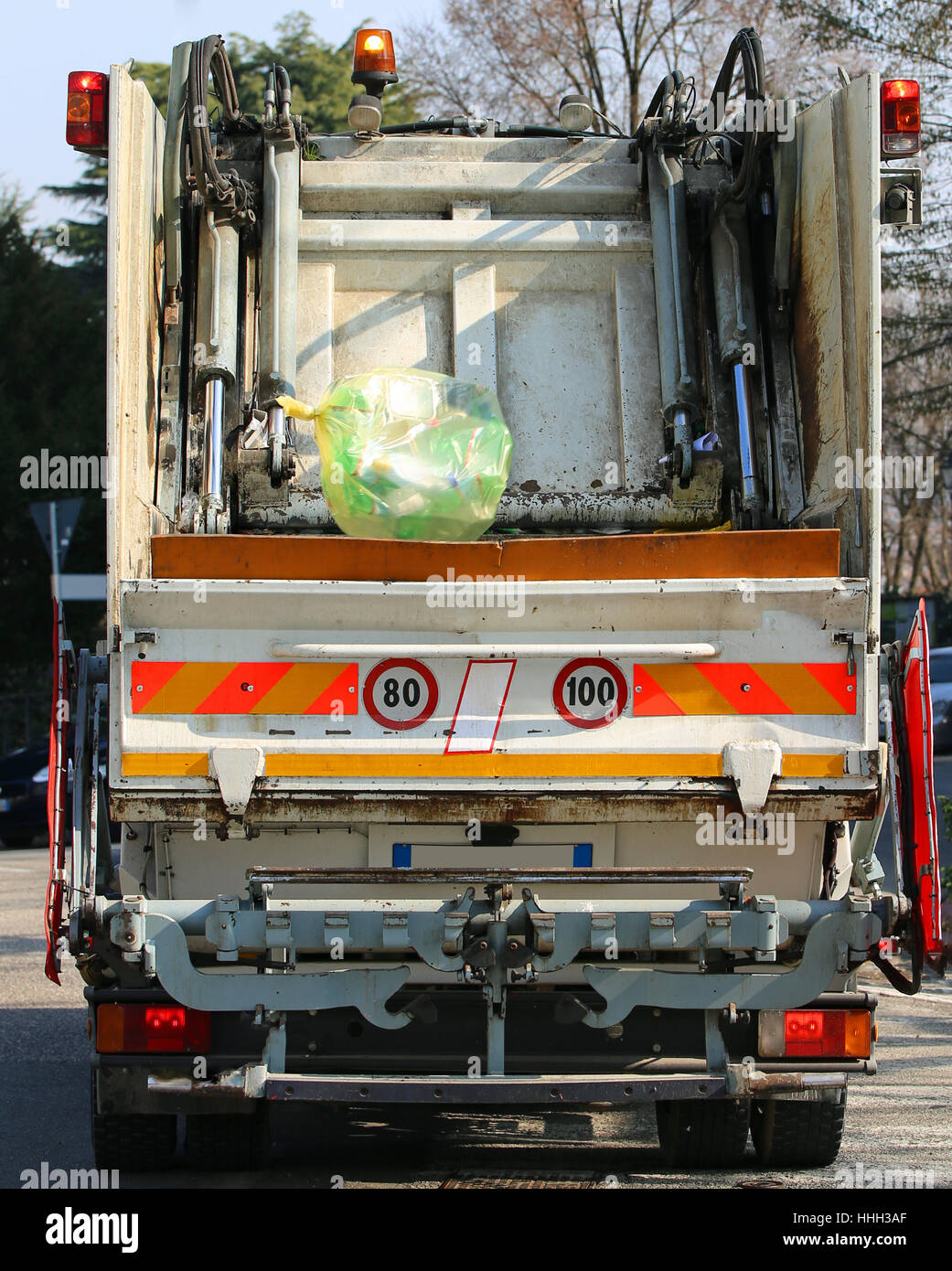 große städtische Hygiene LKW während der Sammlung von festen Abfällen in der Stadt und einer großen gelben Tasche mit Müll Stockfoto